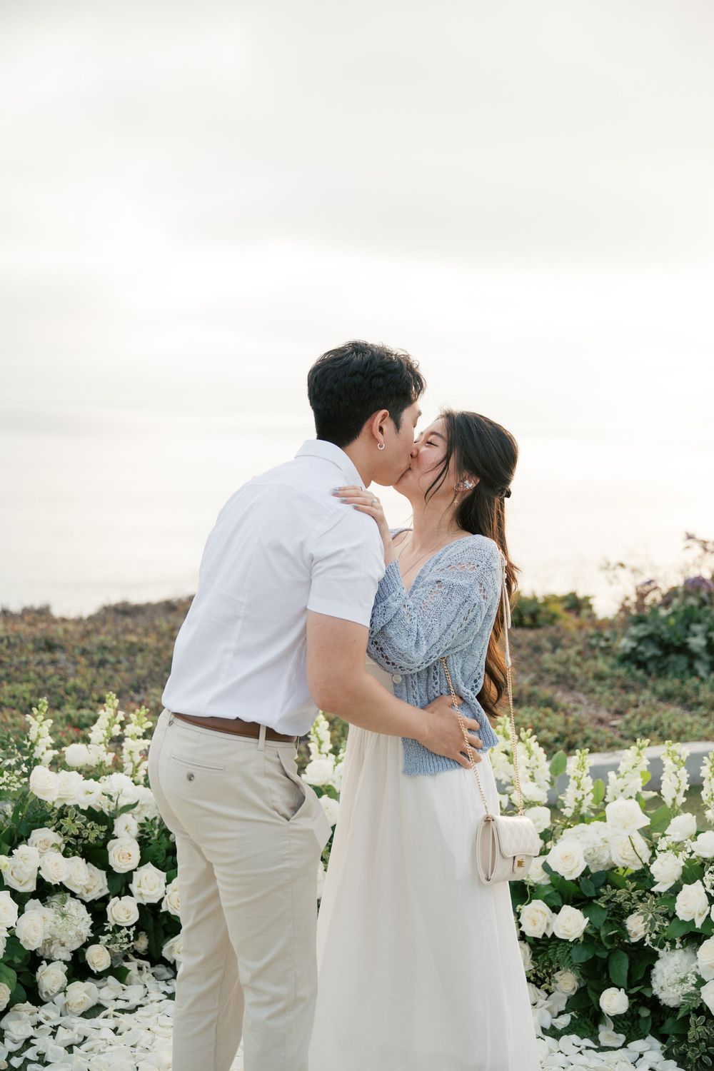 Romantic couple sharing tender moments in a garden of white roses at sunset.