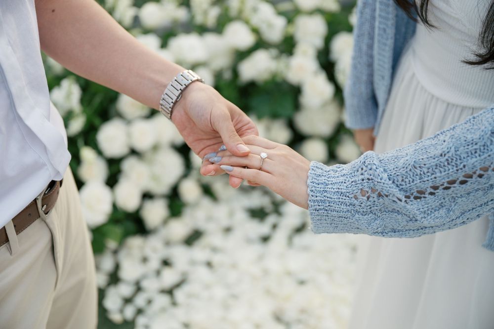 Two people exchange rings during an outdoor wedding ceremony with white flowers in the background.