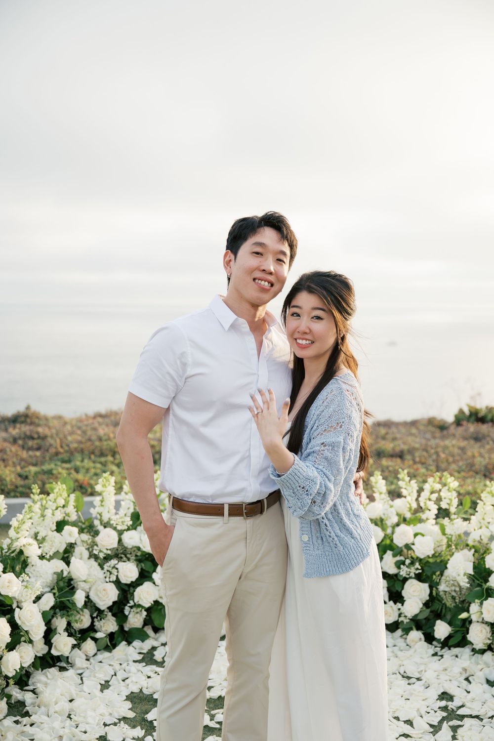 Couple shares intimate moments in a garden filled with blooming white flowers during a romantic photoshoot.