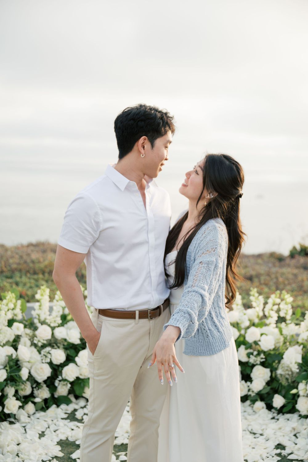 A tender moment between a couple during their engagement shoot amidst white floral arrangements in nature.