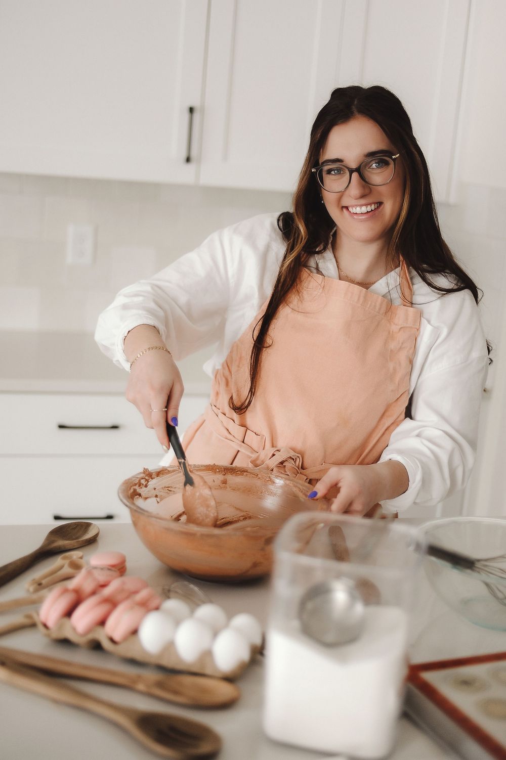 Woman in peach sweater baking and mixing ingredients in kitchen with natural light.