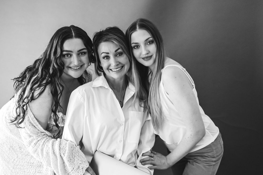 Three women in white shirts share joyful moment together in black and white photography.