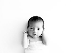 Black and white portrait of an adorable baby in white clothing looking at camera with a gentle expression.