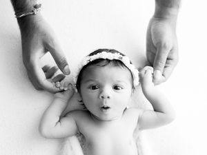 Four black and white photographs of a baby's face being gently touched by adult hands.