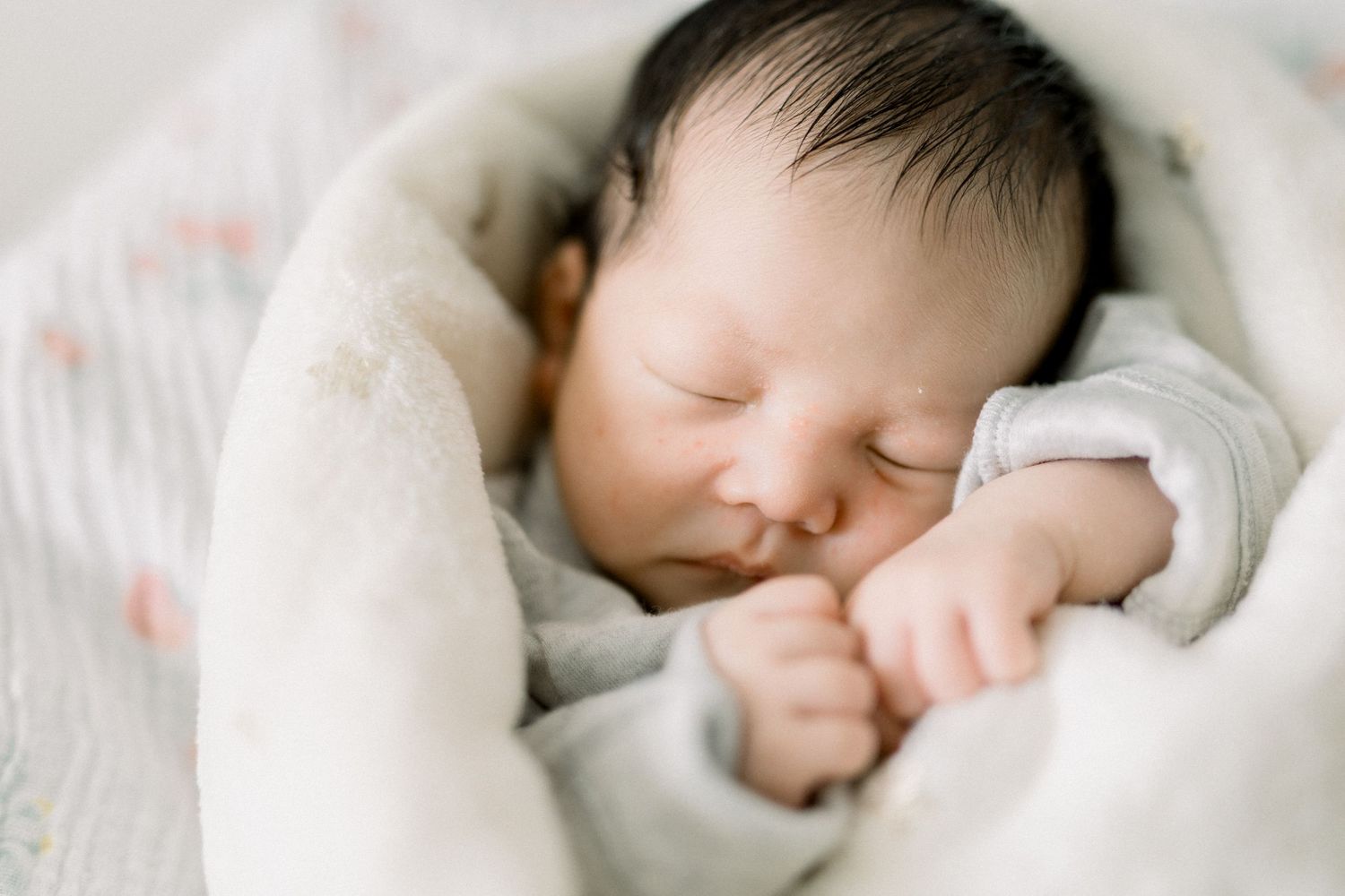 A sleeping newborn swaddled in white blankets rests peacefully against a soft background.