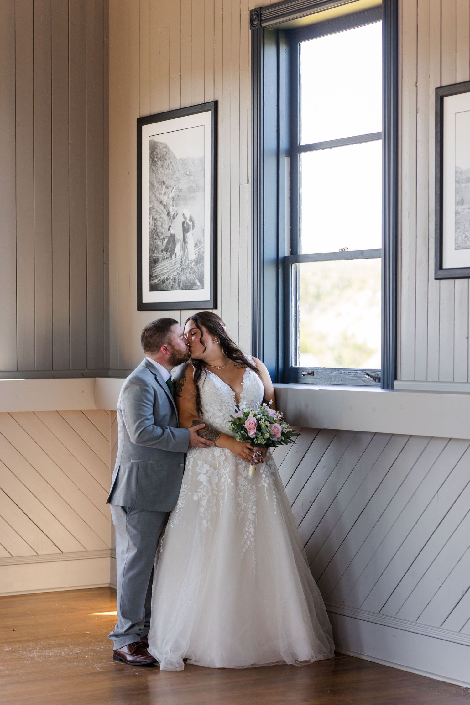 A lovely wedding scene with a couple sharing an intimate moment while holding a pink rose bouquet indoors.