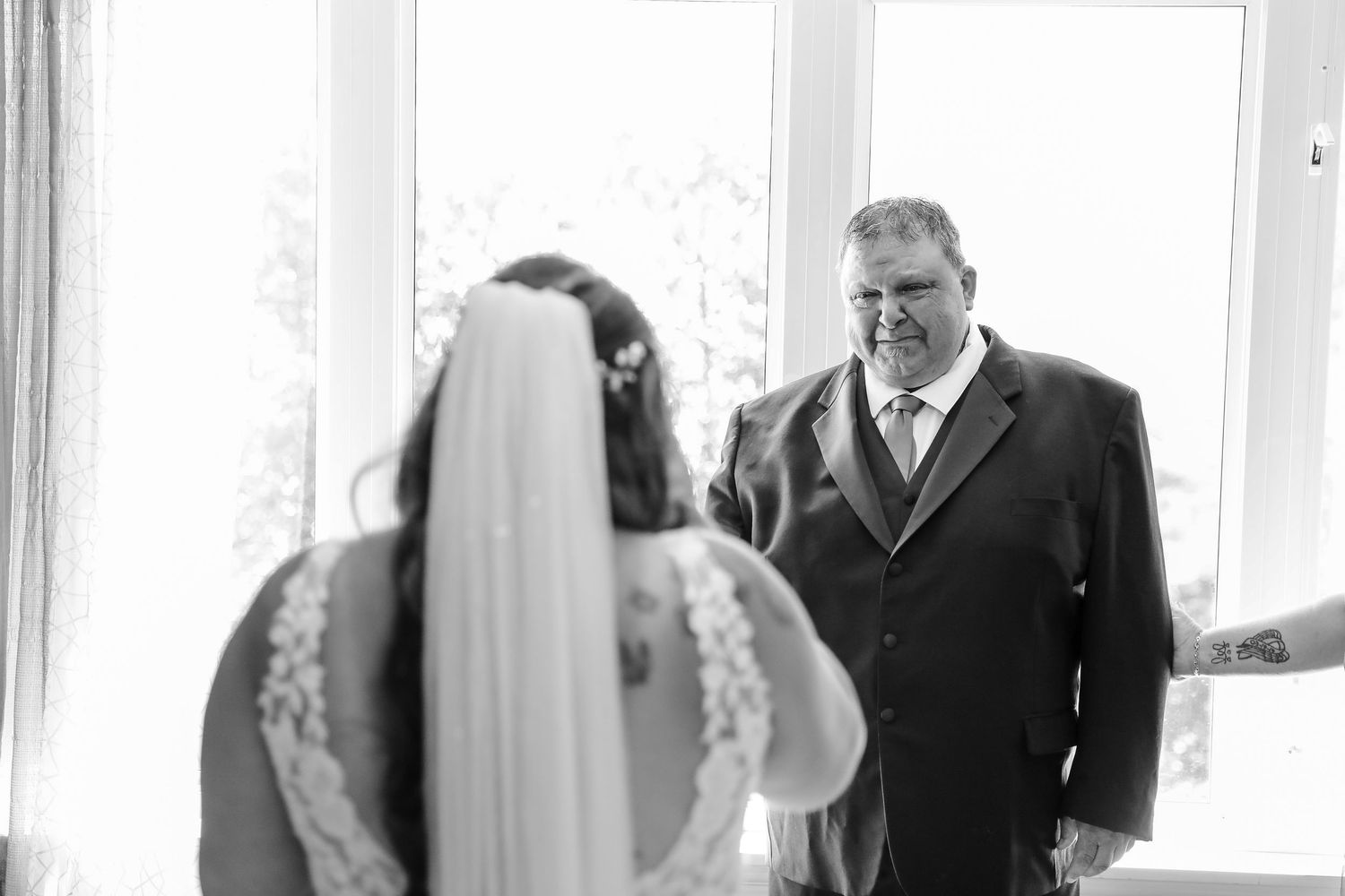 A touching first-look moment between a bride in a lace veil and someone in a dark suit during a wedding ceremony.