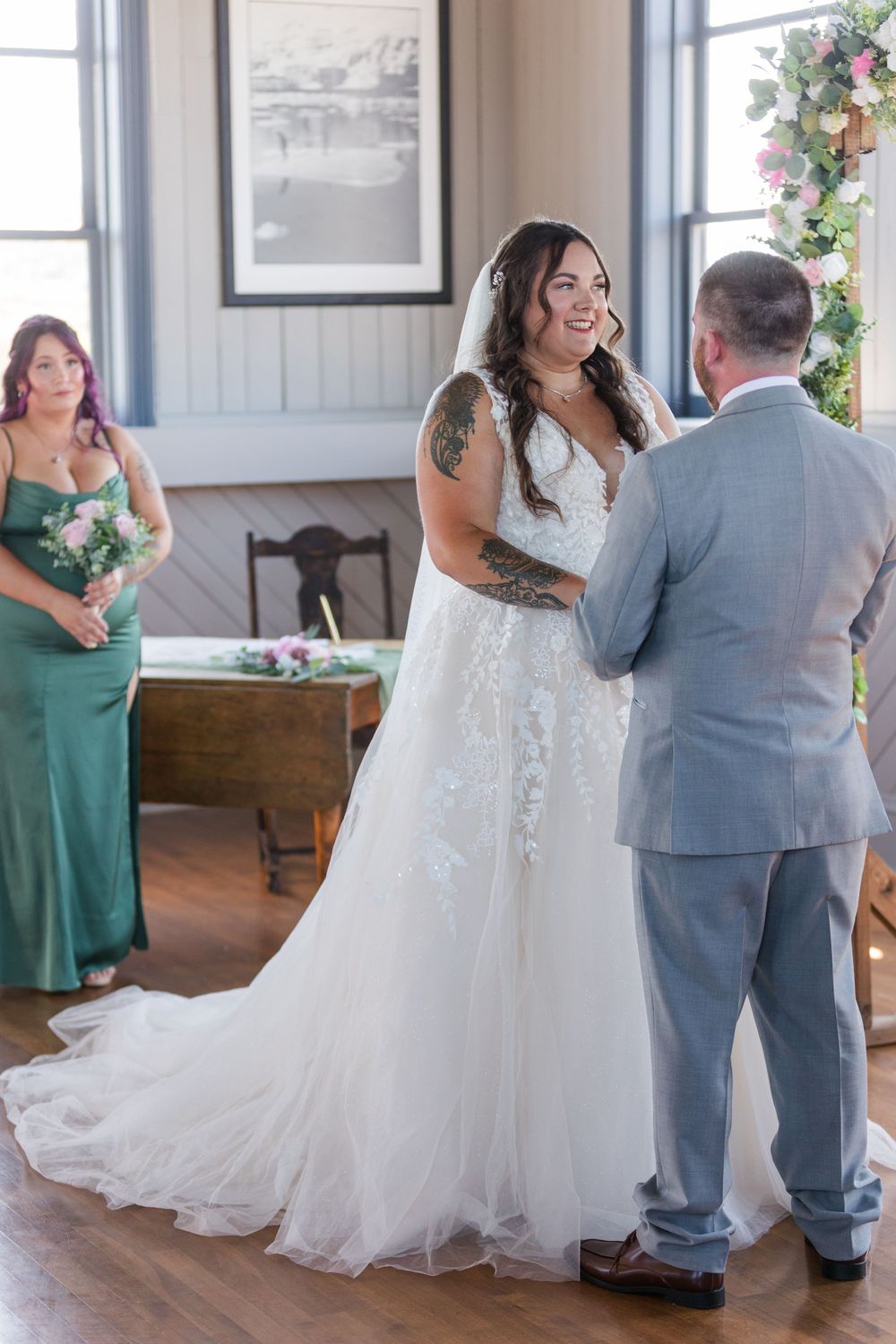 Wedding ceremony in a rustic venue with couple exchanging vows as a bridesmaid in emerald green looks on.