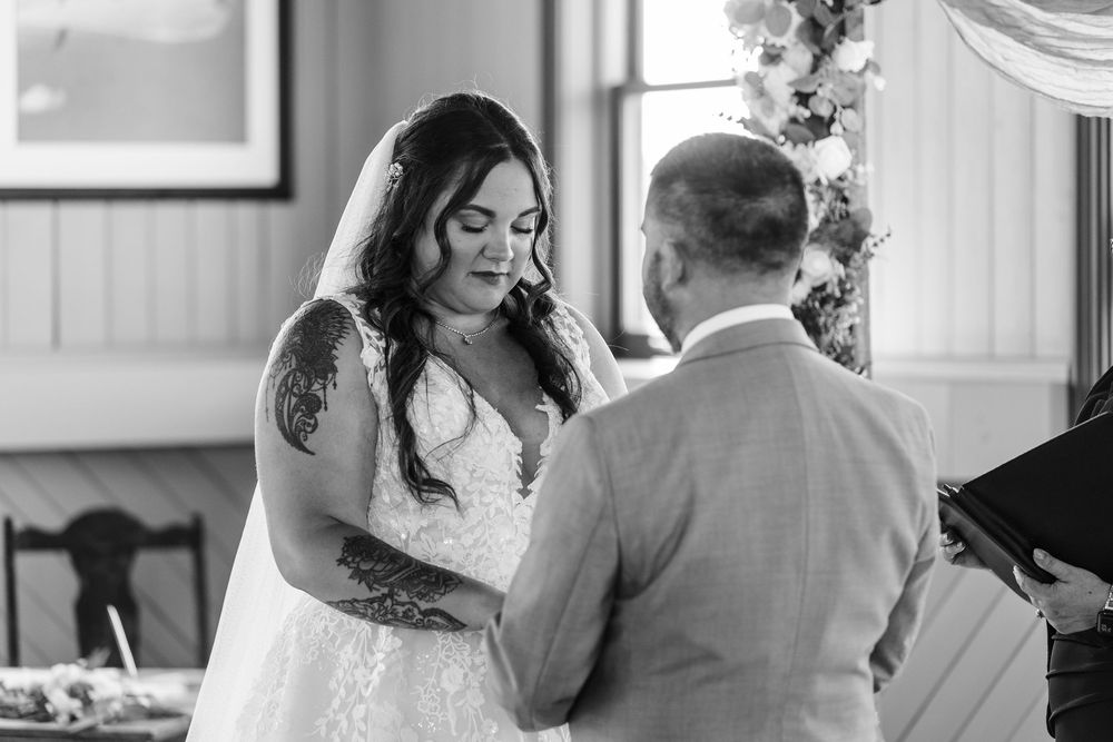 A black and white photograph captures an intimate wedding ceremony moment between a couple exchanging vows.