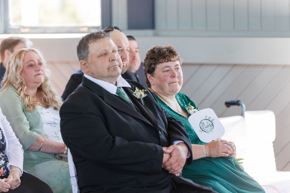 Wedding guests smile and share an emotional moment while seated during an outdoor ceremony.