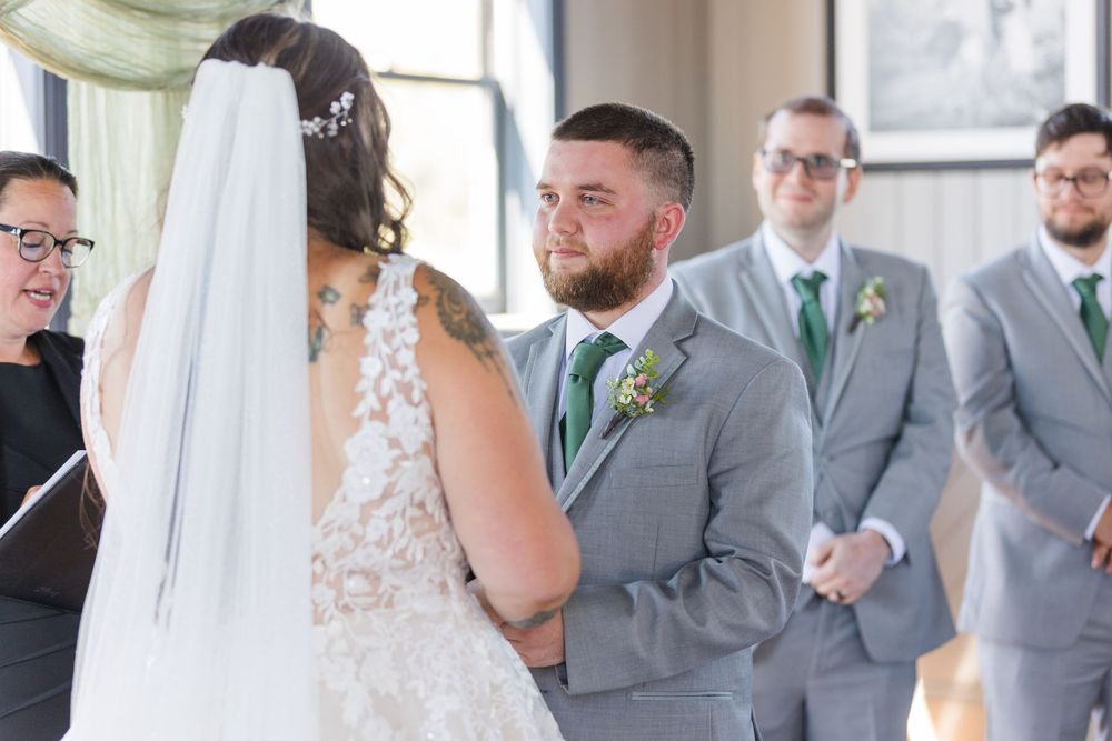 A couple exchanges vows during their wedding ceremony as groomsmen in gray suits with green ties look on.