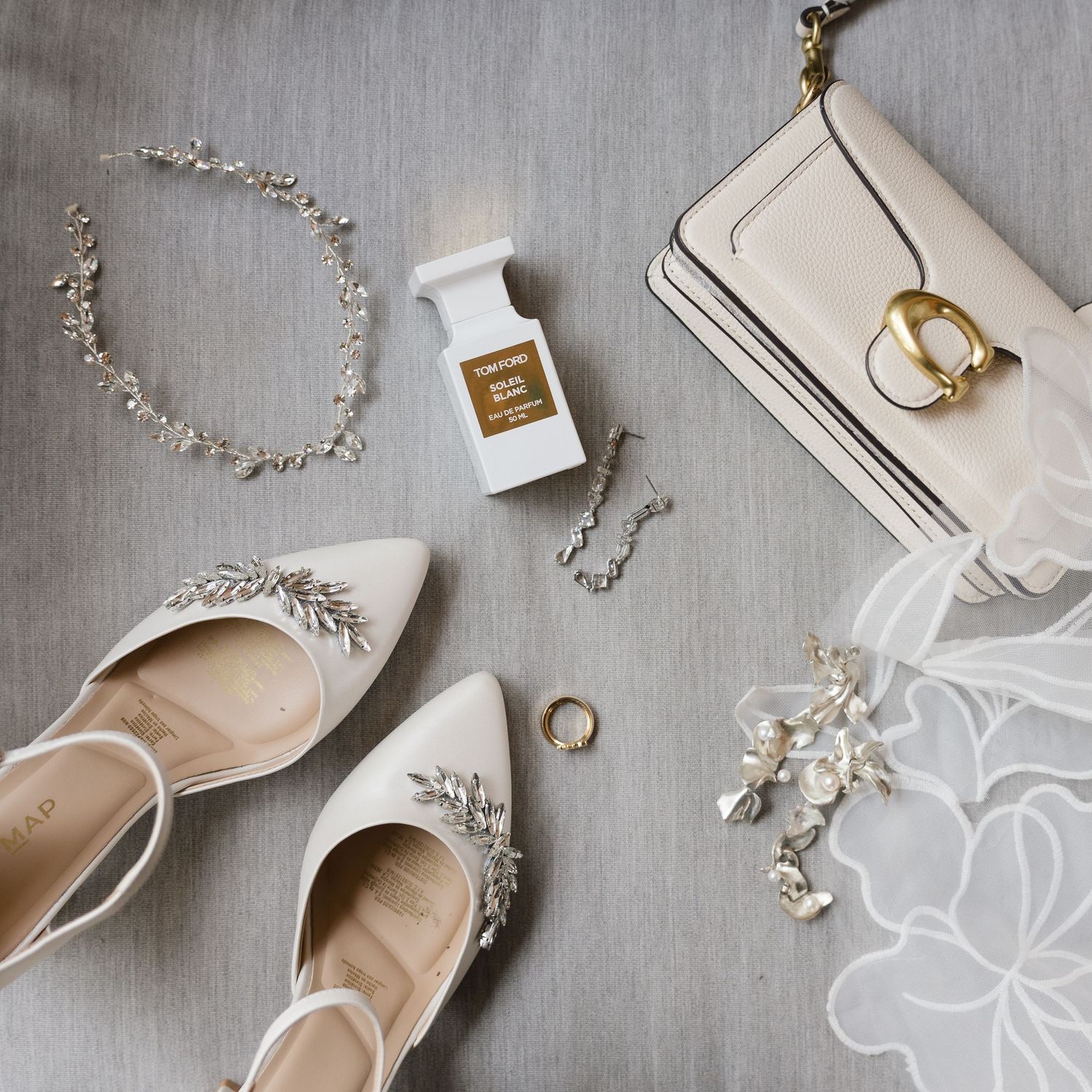 Wedding accessories including delicate jewelry, shoes, and rings arranged on a light gray background.