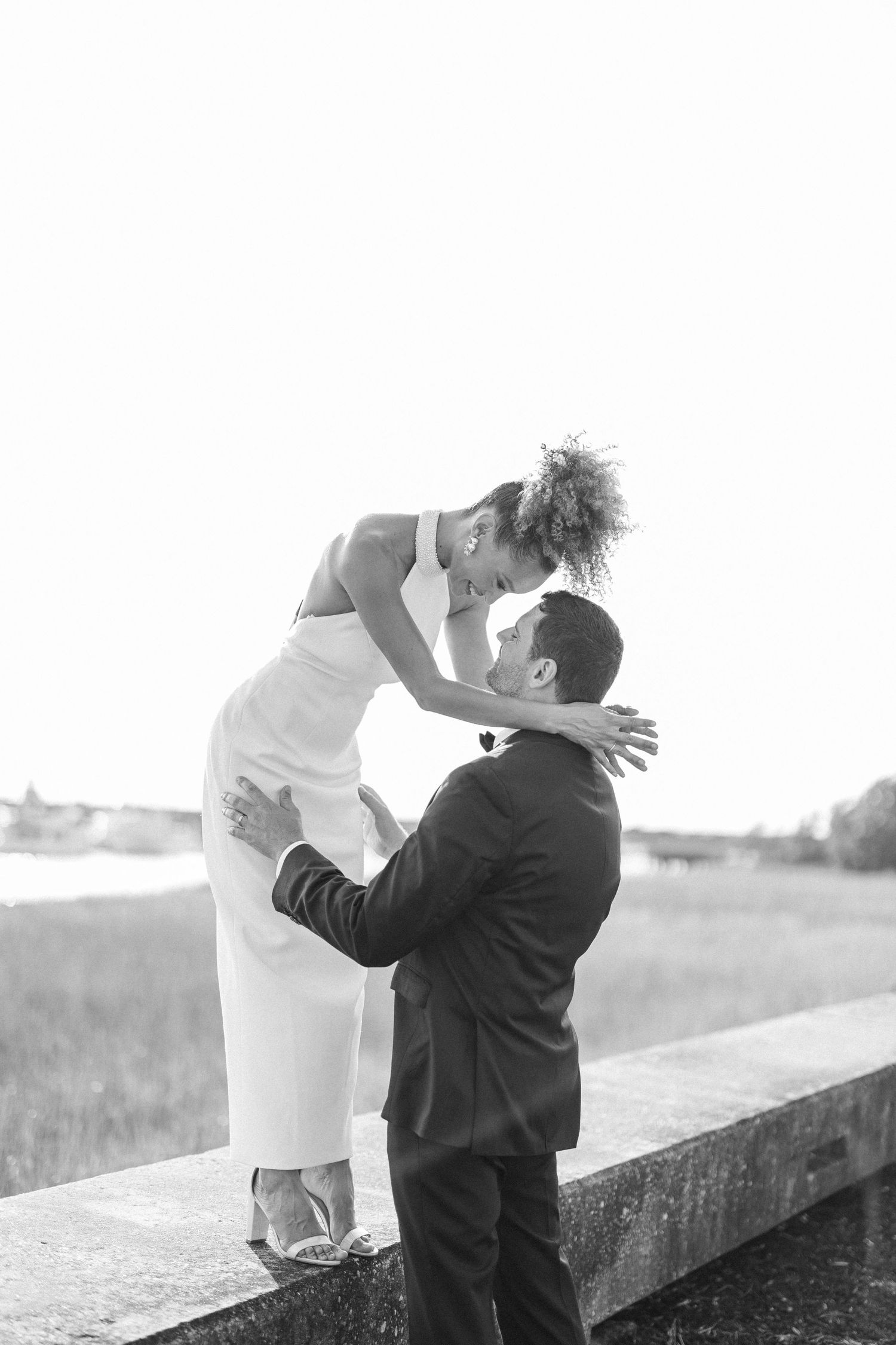 A romantic black and white photo series showing playful moments between a bride and groom on a retaining wall.
