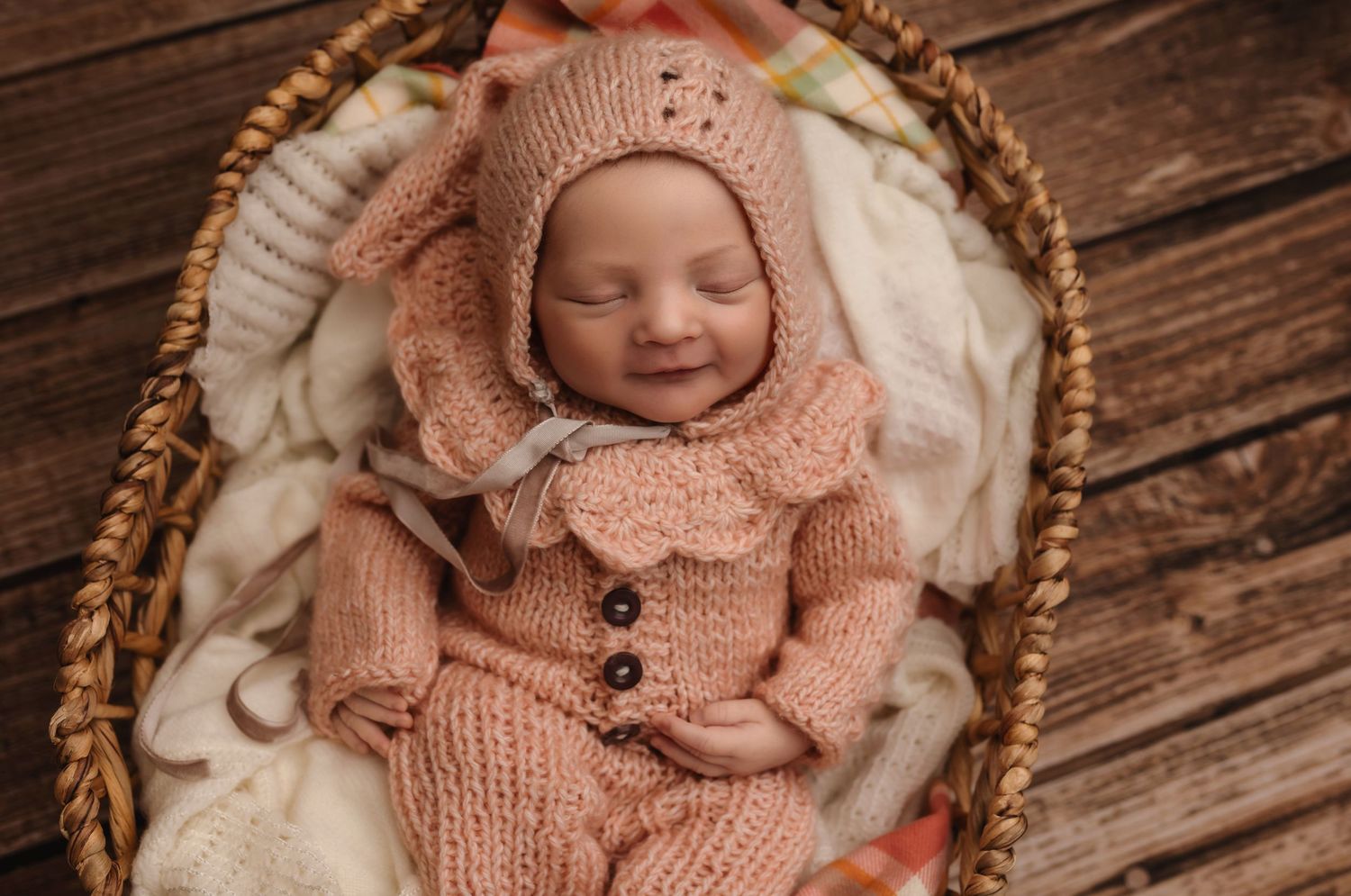 Sleepy baby girl smiles and is dressed in a peachy knit outfit with matching hat, captured by Charlottesville newborn photographer.