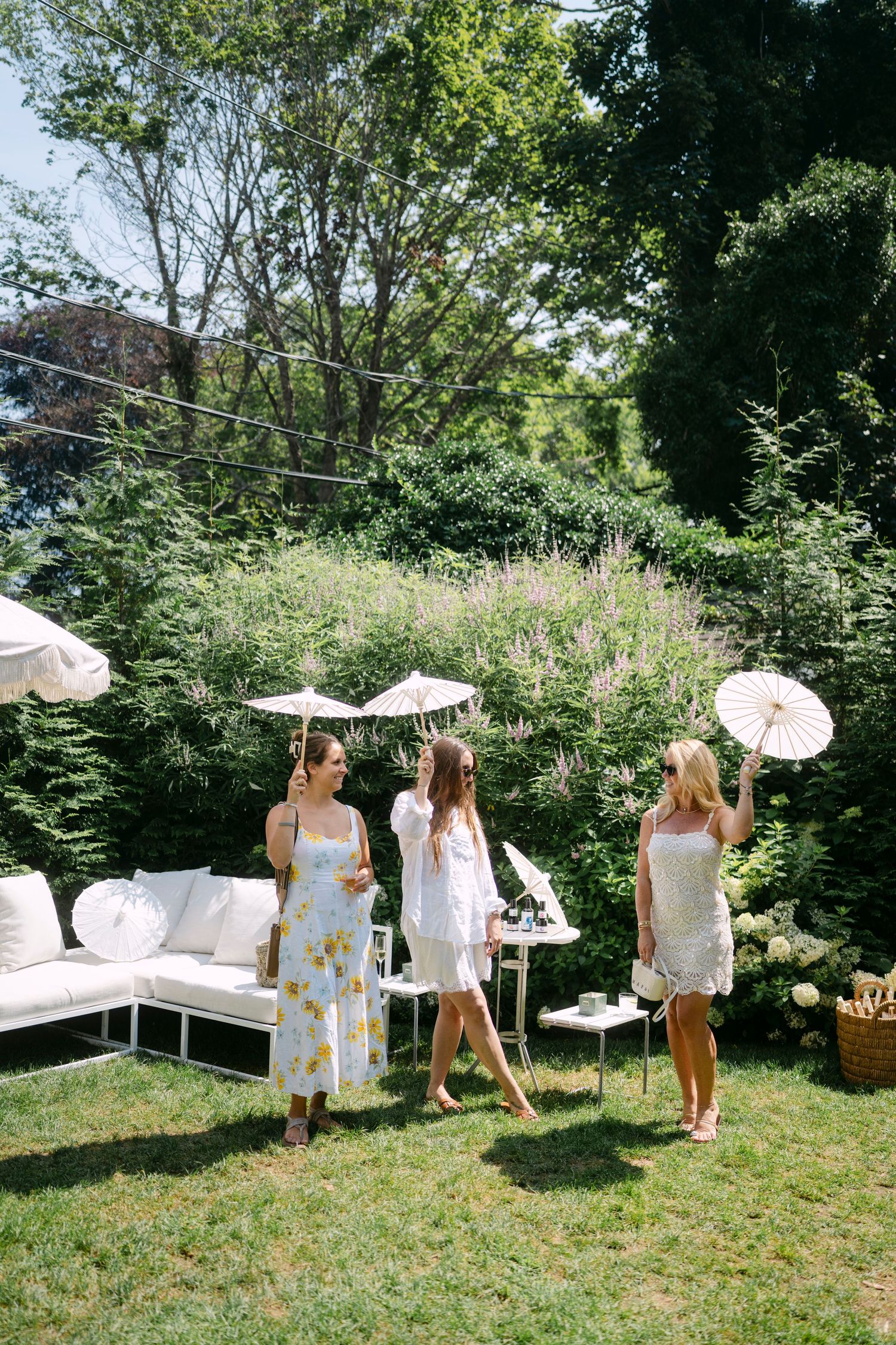 Ladies in summer dresses enjoying an outdoor garden party with white parasols.