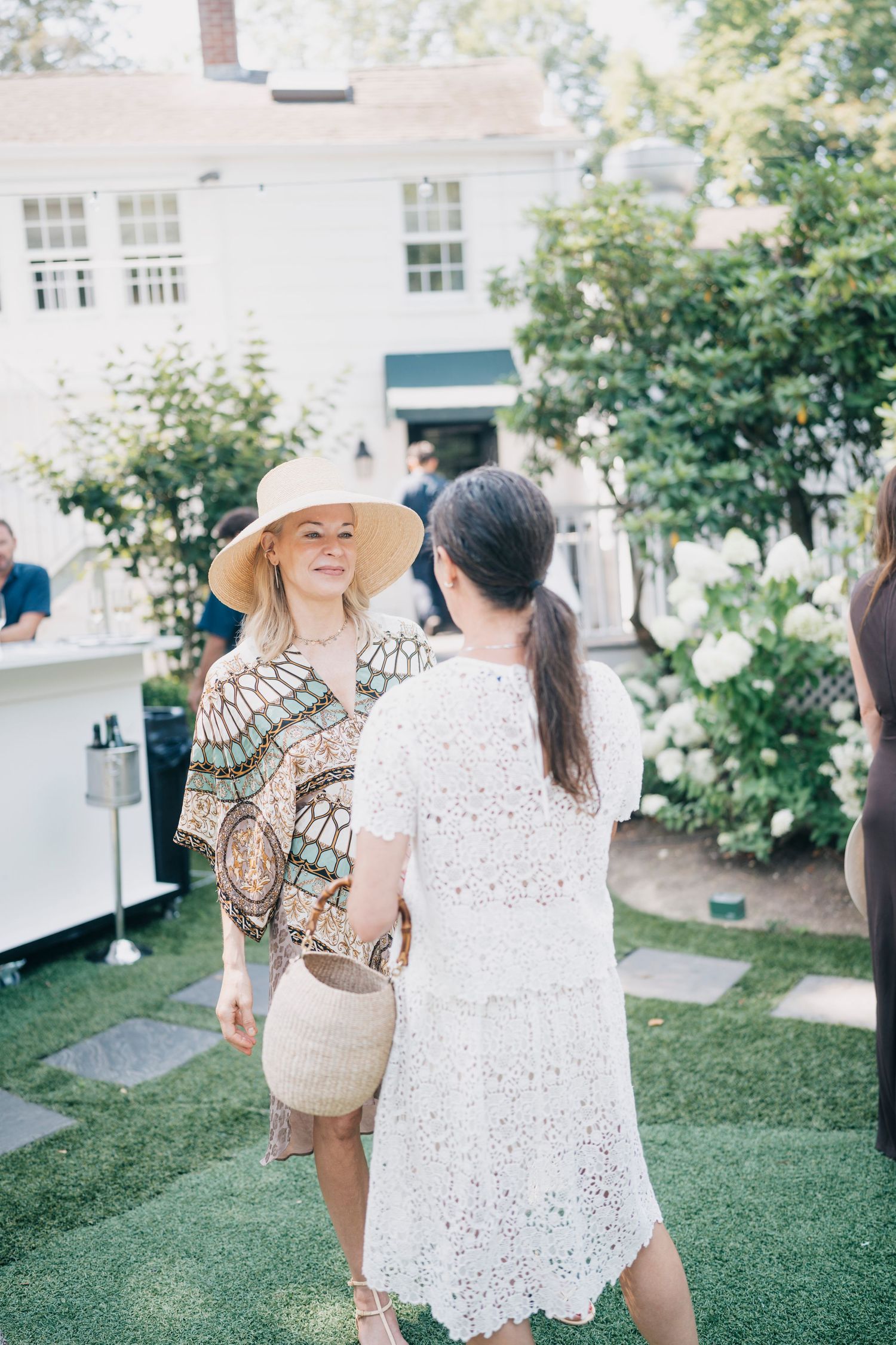 Women in summer dresses and hats gathering on a lawn during an outdoor social event.