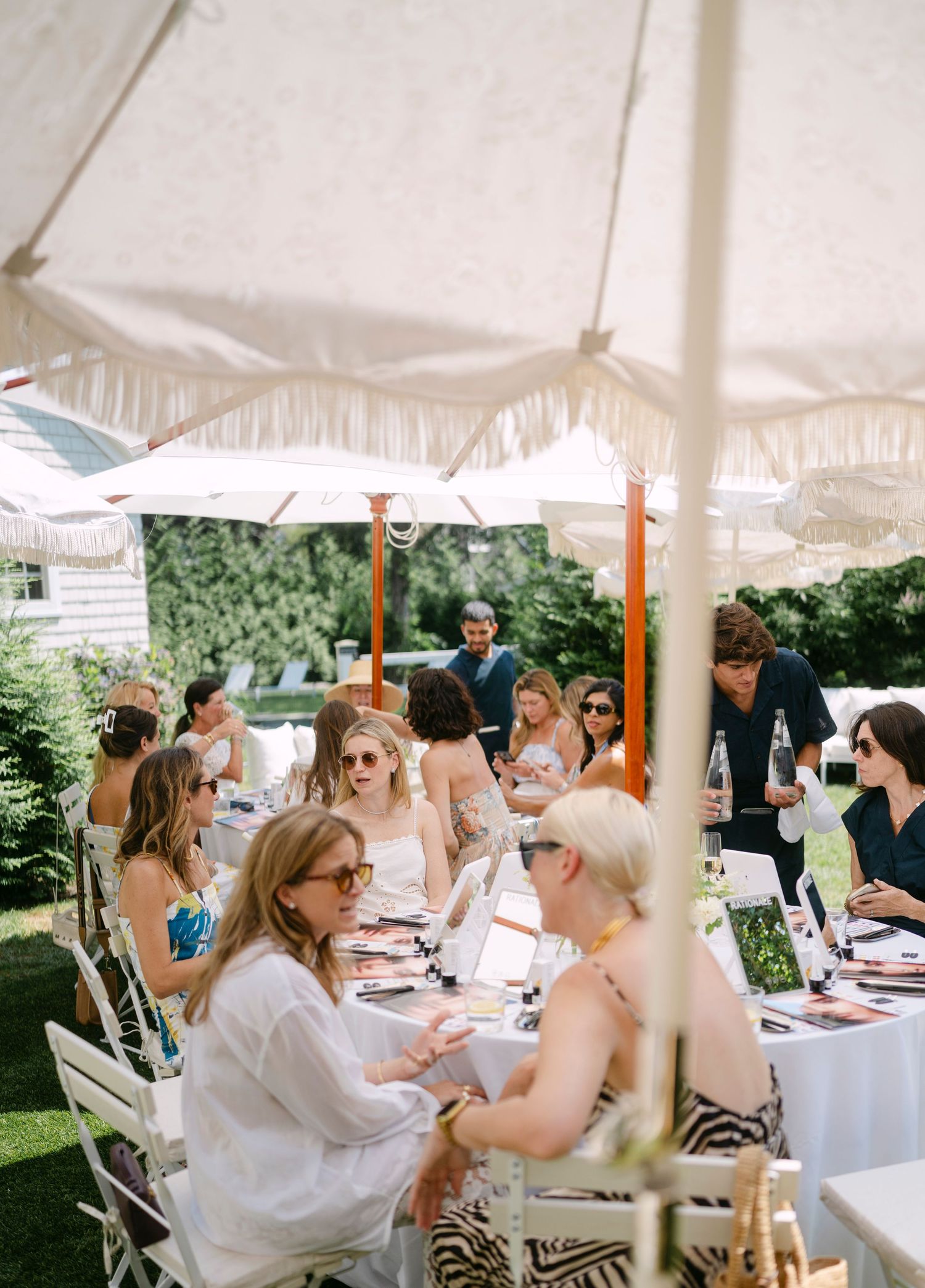 Outdoor garden party setting with white umbrellas and tables where guests gather for a special event.