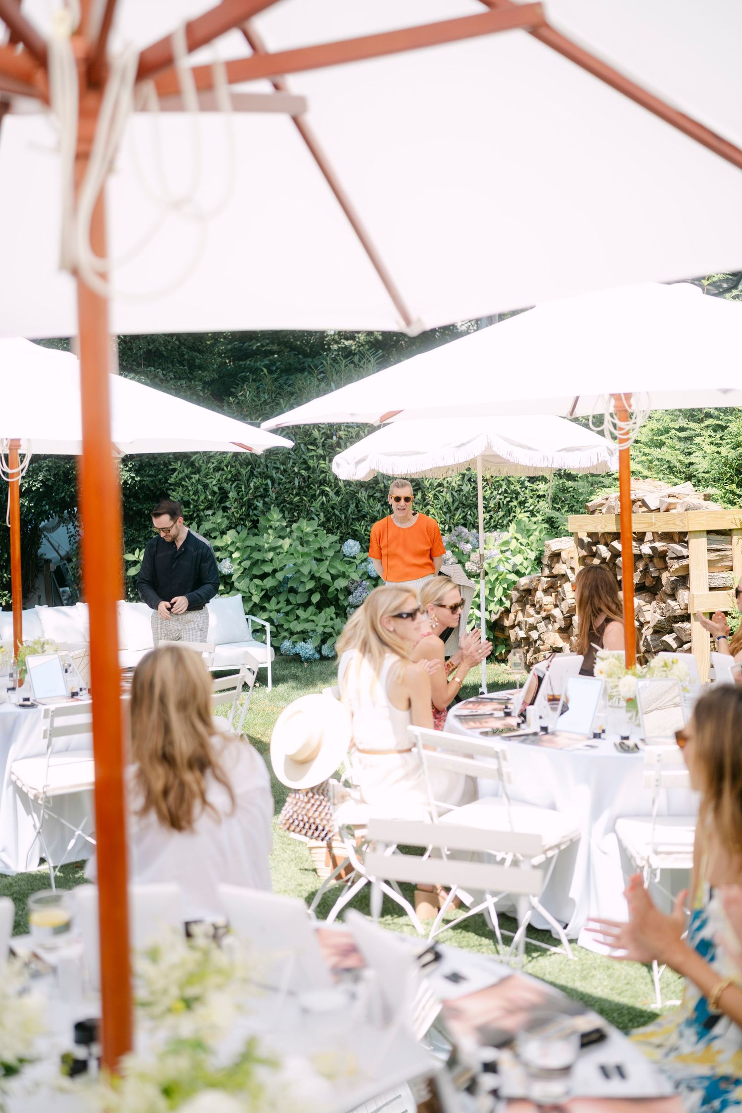 White tent covered outdoor gathering with guests seated at tables in a lush garden setting.