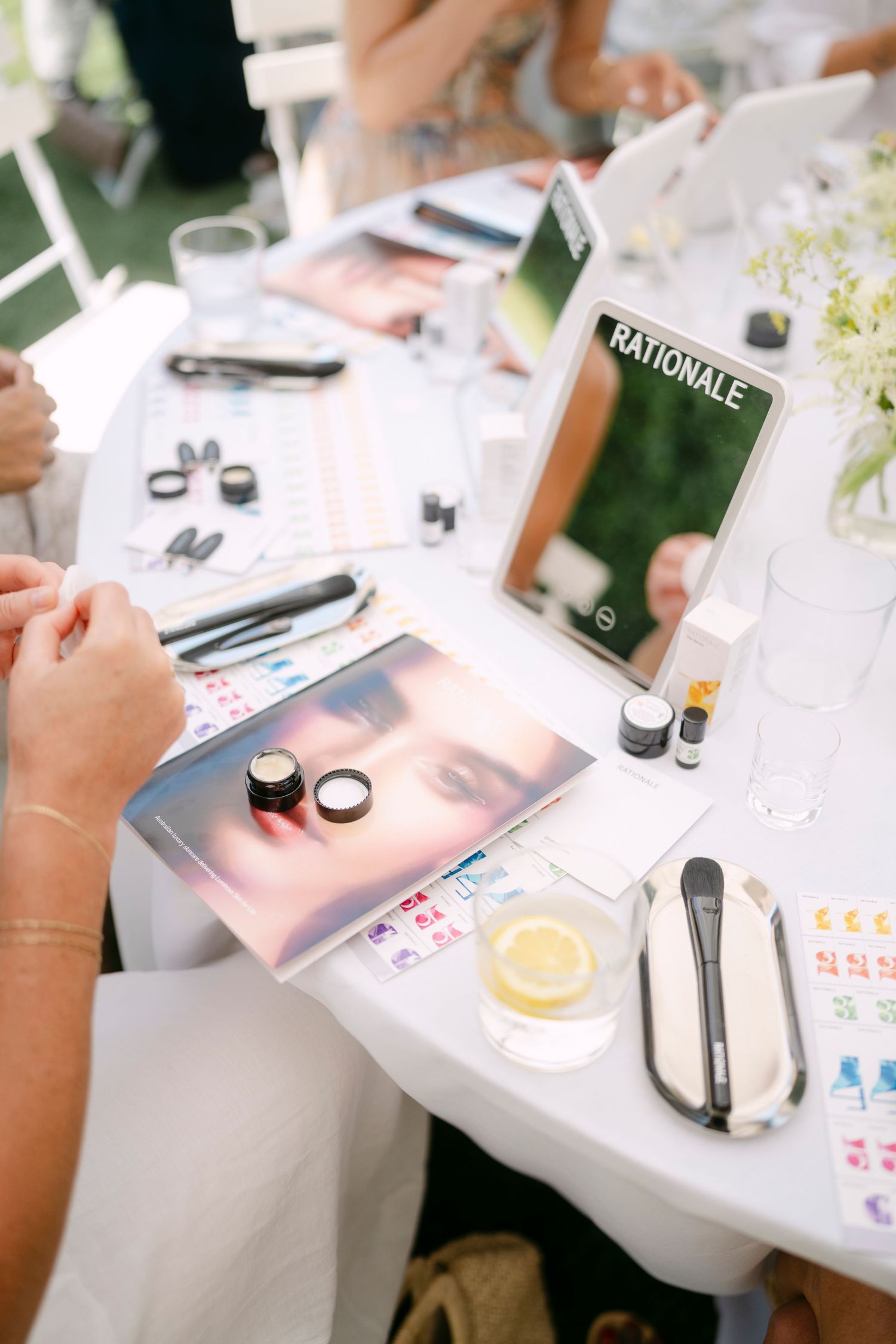 Close-up view of beauty and cosmetic products scattered on a white table during an outdoor event.