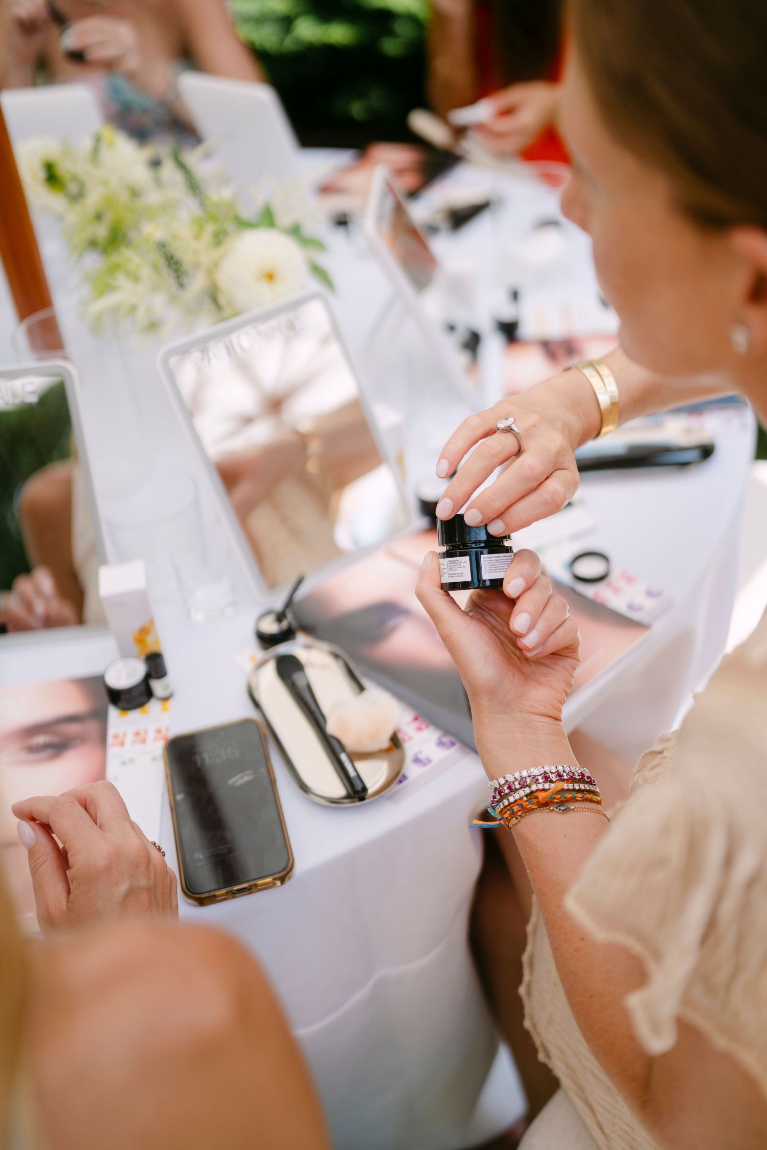 Hands holding makeup products and samples at an outdoor beauty demonstration event.