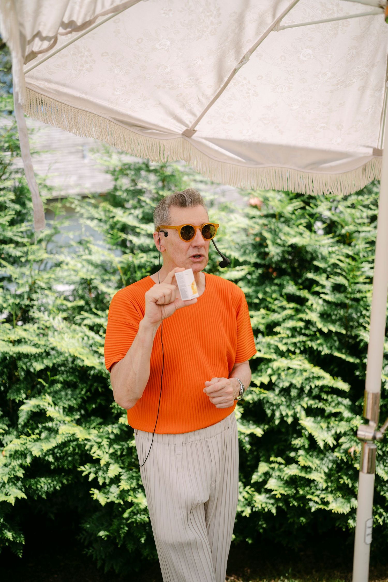 Person in orange top and sunglasses enjoying refreshments under a white tent at an outdoor event.