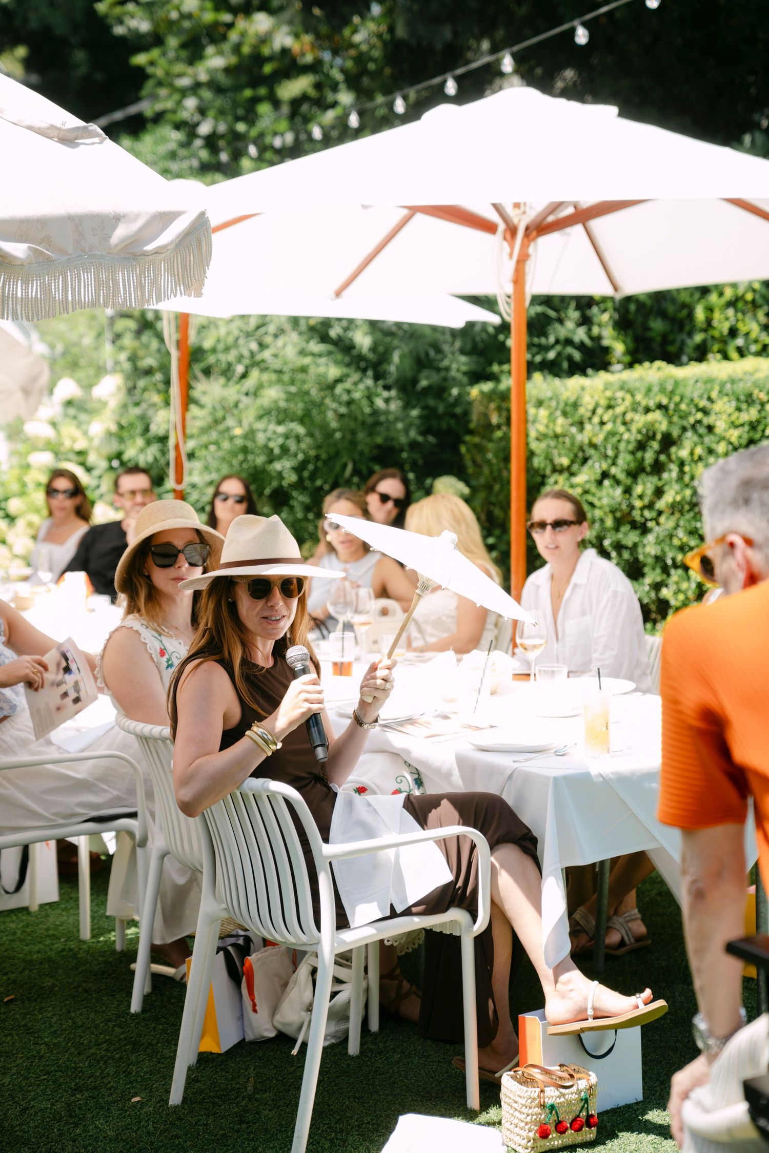 Guests enjoy a shaded outdoor dining setup with white umbrellas and tablecloths in a garden setting.