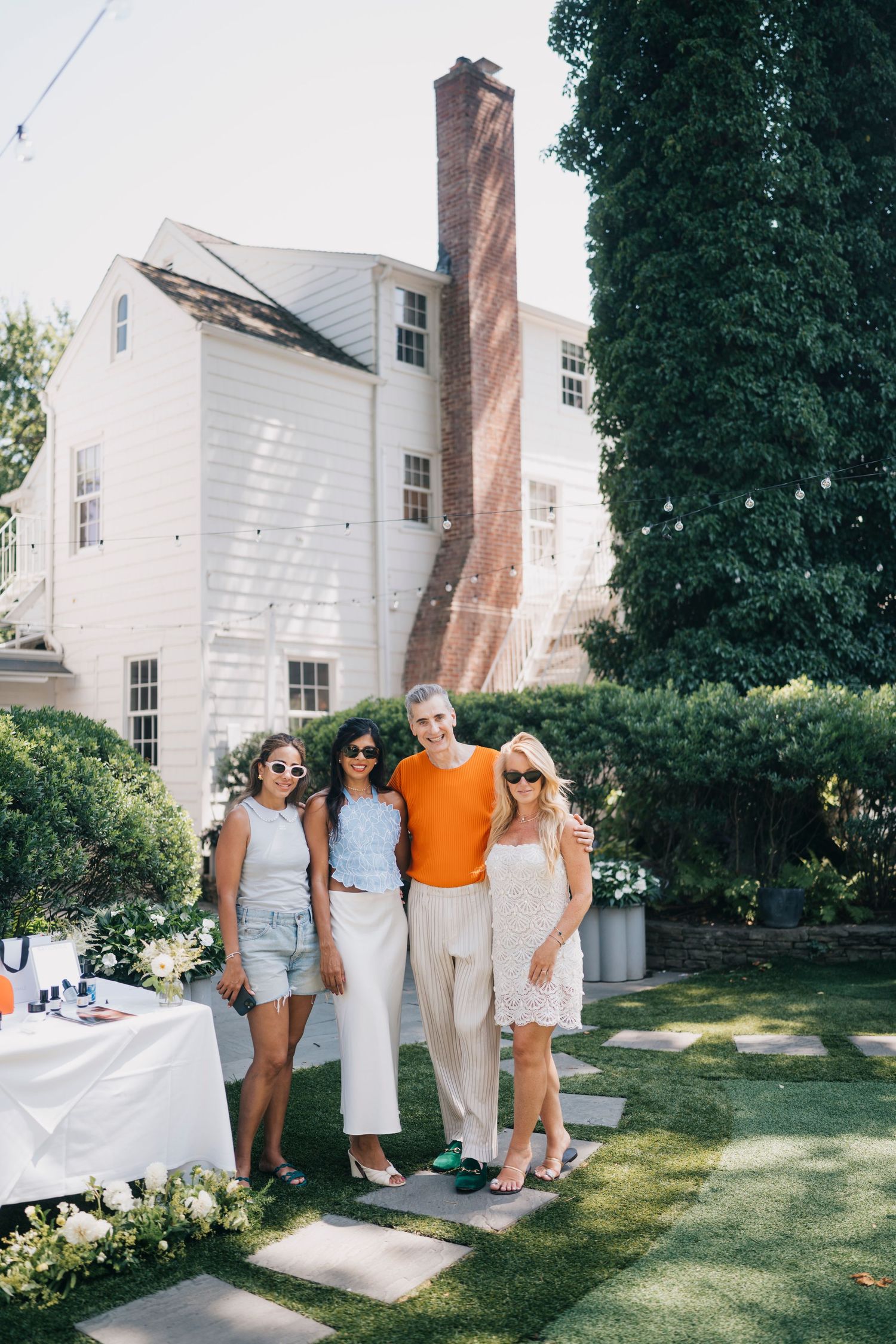 A group poses for a photo in front of a white colonial-style house during a summer party.