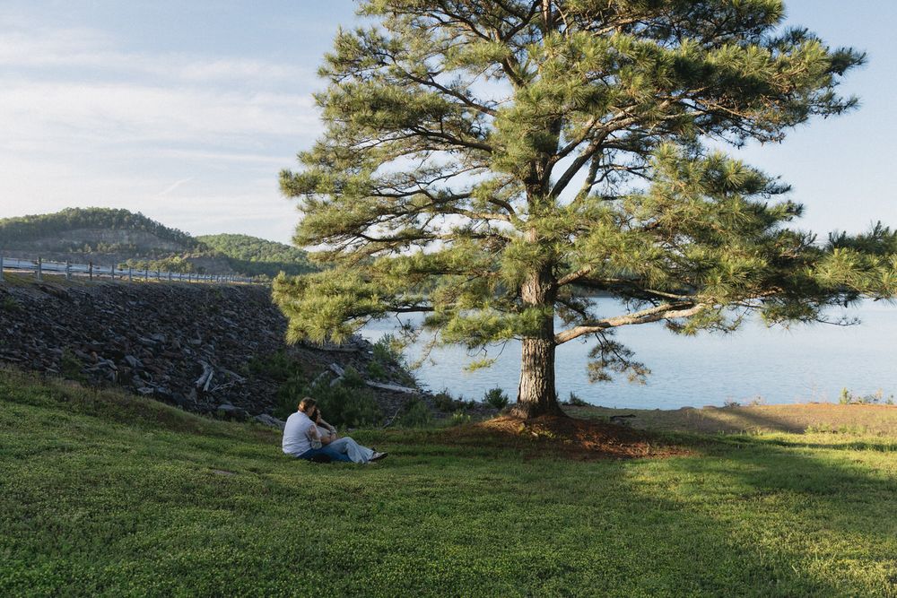 A wide shot of two fiancés, cuddling under a tree during their North Georgia engagement session at Carter's lake dam.