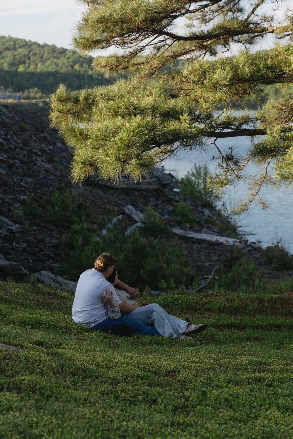a couple cuddles underneath a tree during their North Georgia engagement session. The photo is it true to life showing the sunset.