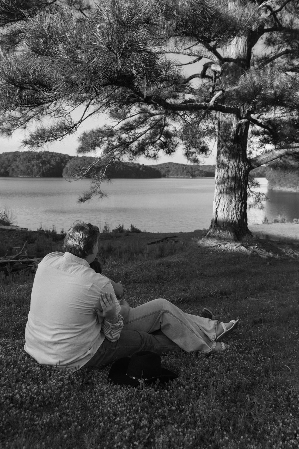 A black-and-white image of a man holding his bride to be underneath the tree at Carter's lake dam