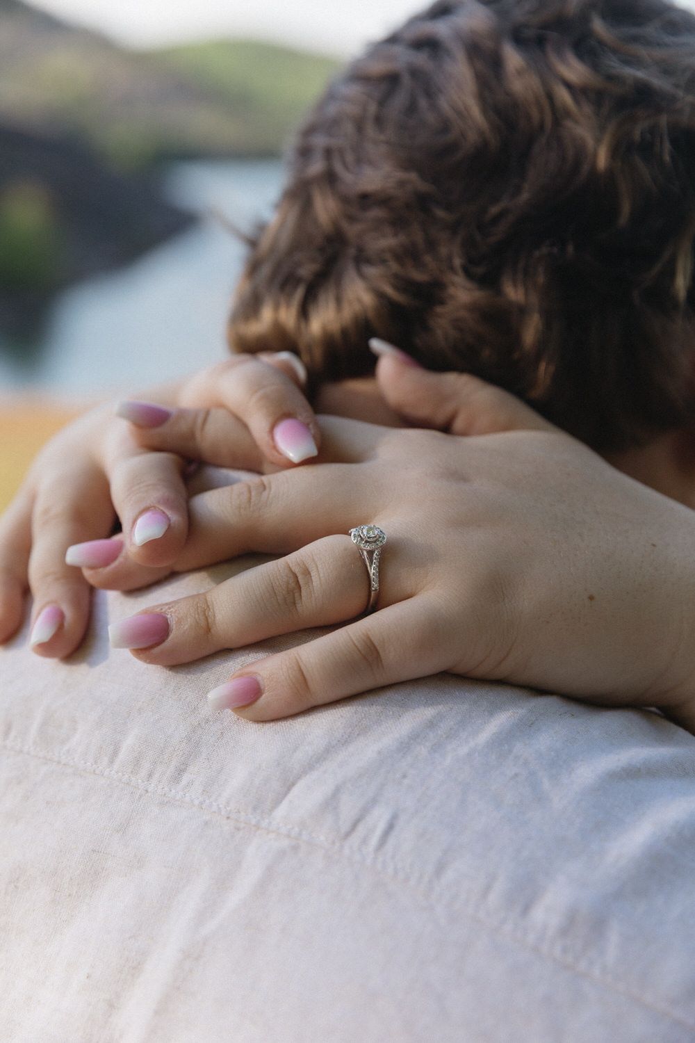 Close-up of hands clasped together featuring a delicate engagement ring with a round solitaire diamond.