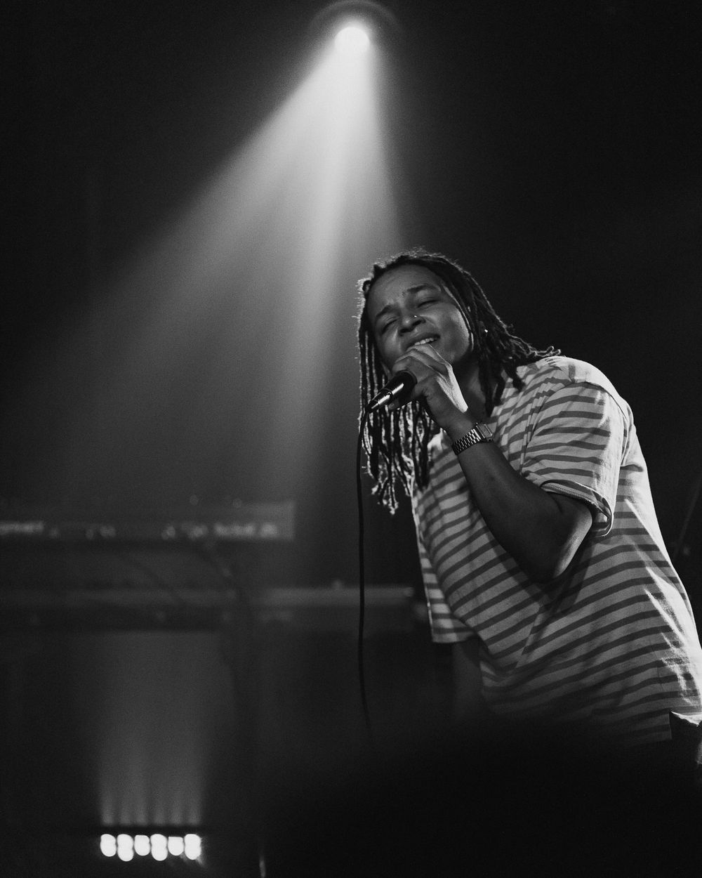 Dramatic black and white performance photos showing a singer in a striped shirt under spotlights on stage.