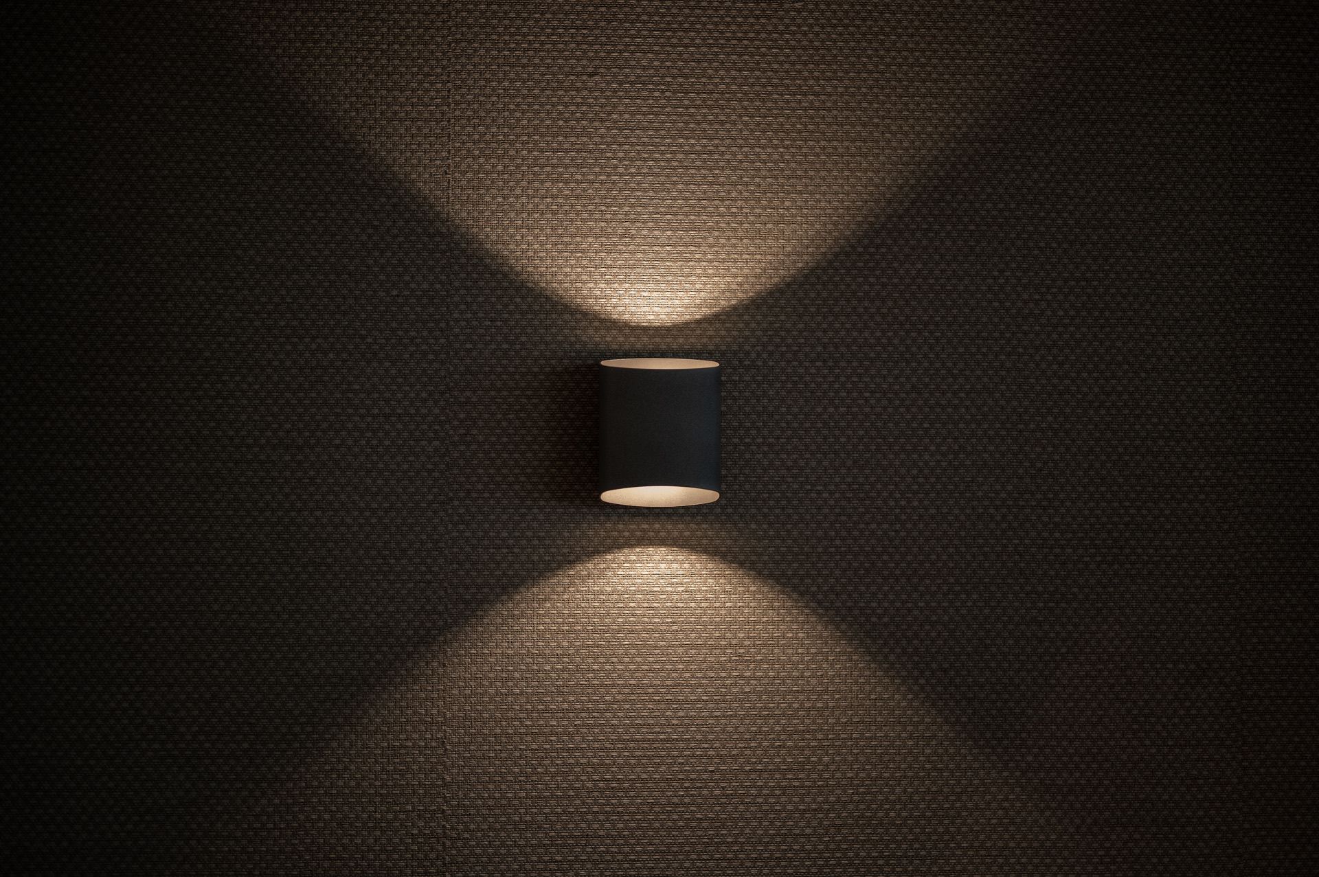 A modern wall sconce casts dramatic up and down light patterns on a dark textured wall in the Algarve, by Parallel Studios