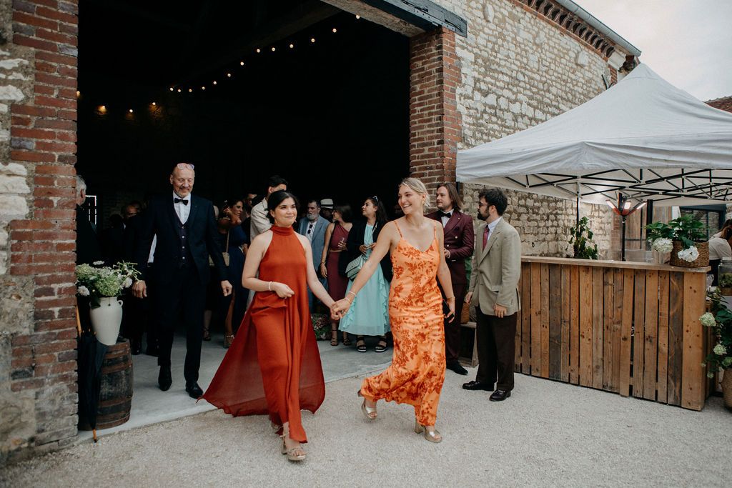 Wedding guests in colorful dresses exit a rustic barn venue during an outdoor celebration.