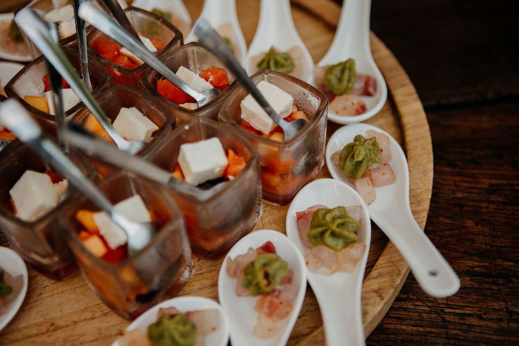 Elegant wedding appetizers including bruschetta cups and garnished spoons arranged on a wooden board.