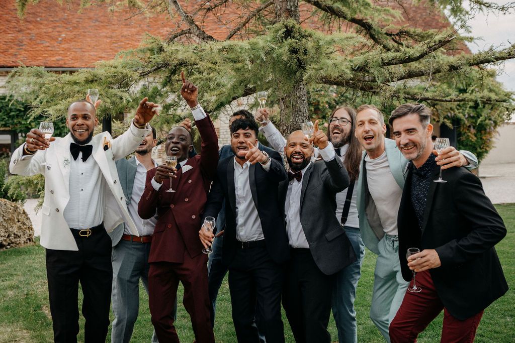 A joyful group of groomsmen in stylish suits celebrate outdoors at a wedding reception.