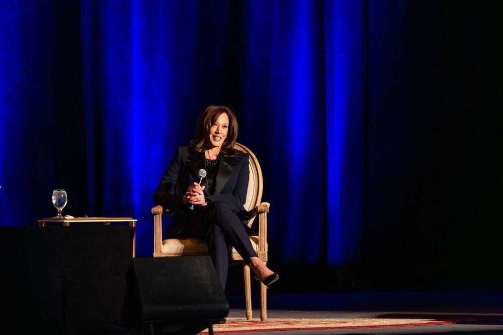 A speaker stands at a podium on stage with dramatic blue lighting and dark background during a presentation.