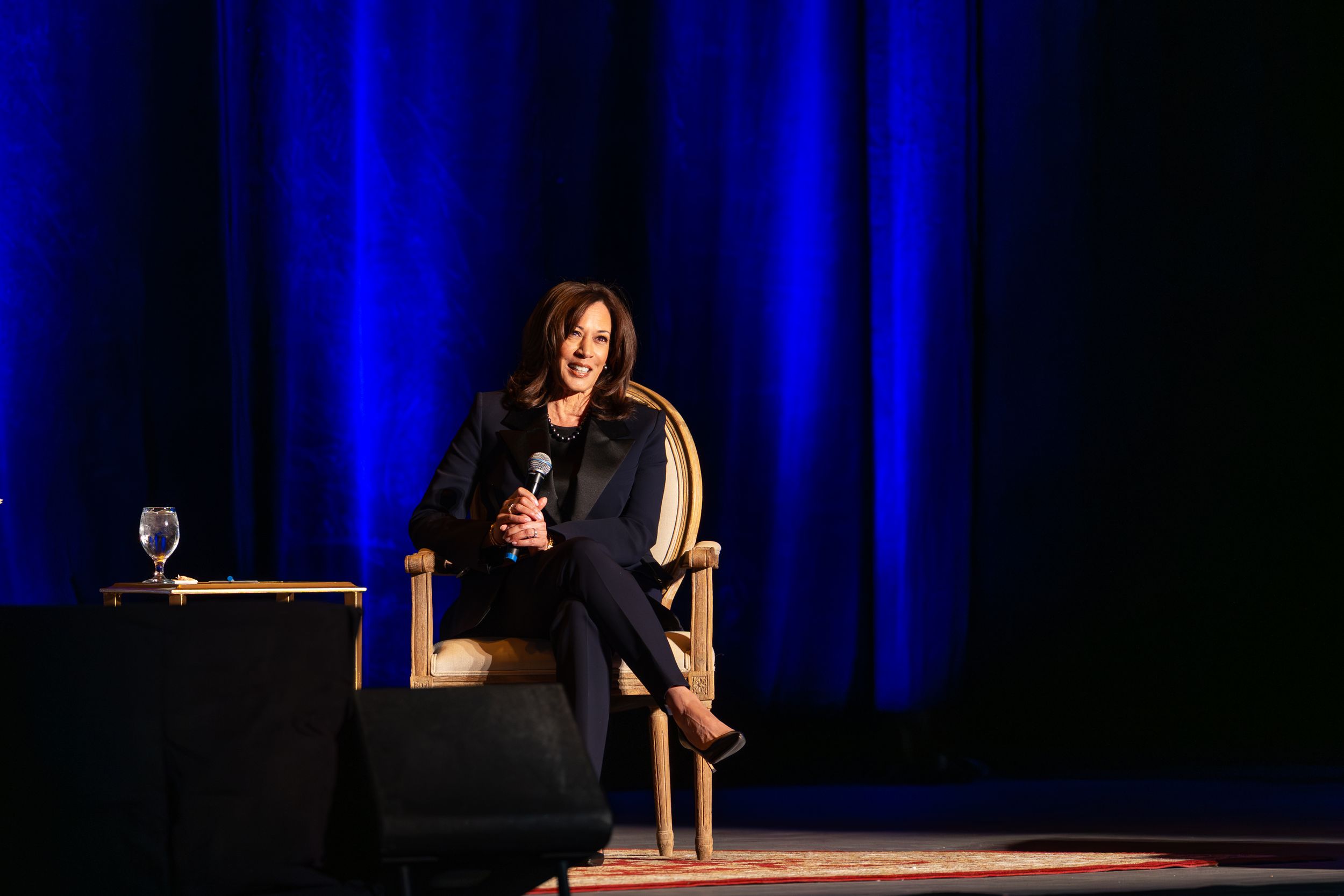A speaker stands at a podium on stage with dramatic blue lighting and dark background during a presentation.