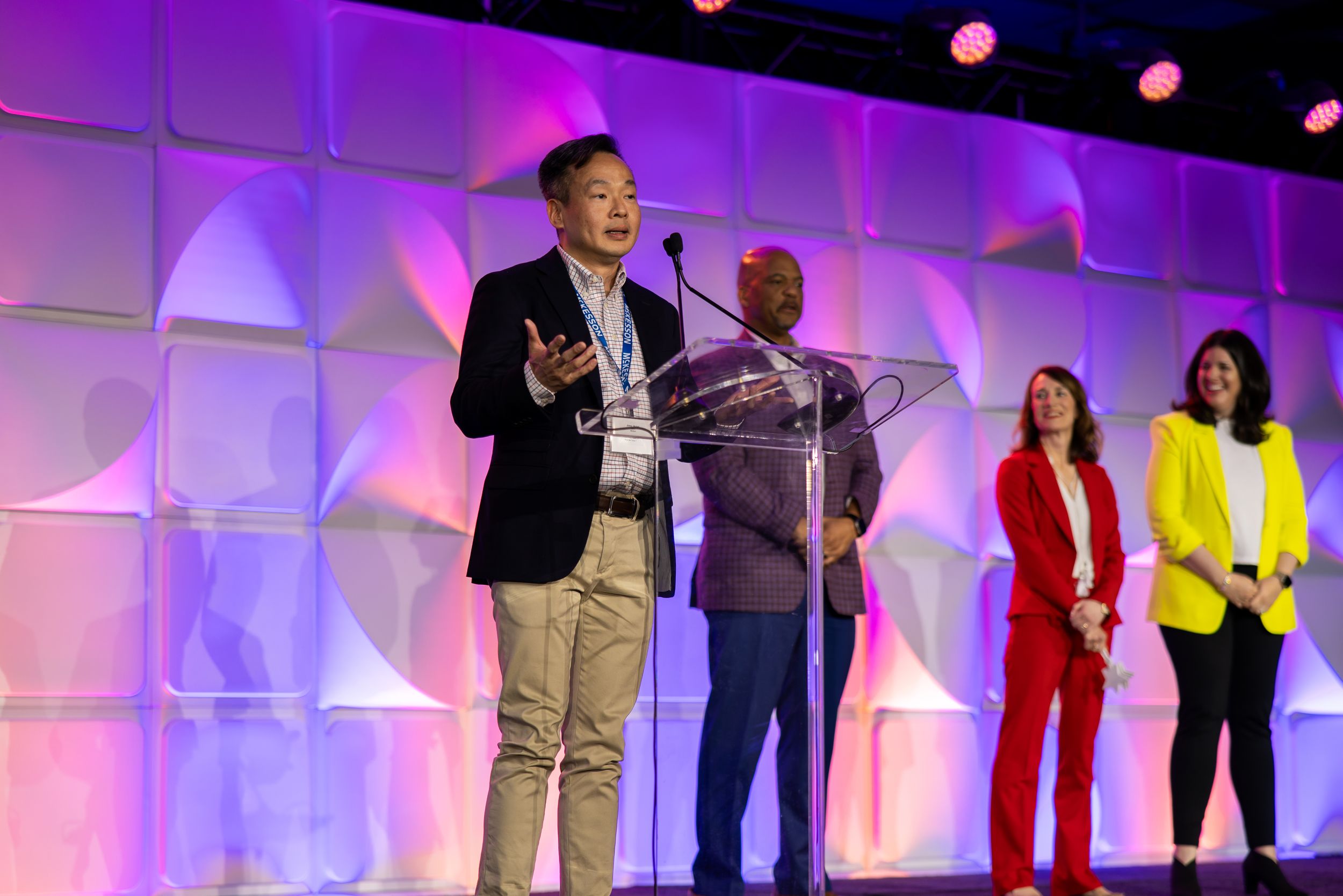 Conference stage setup with purple and pink ambient lighting and multiple presenters.