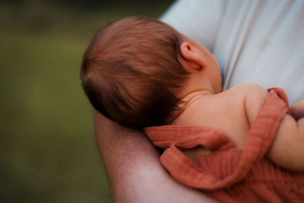 Newborn baby cradled in mother's arms, photographed with soft, moody lighting to highlight emotional connection.