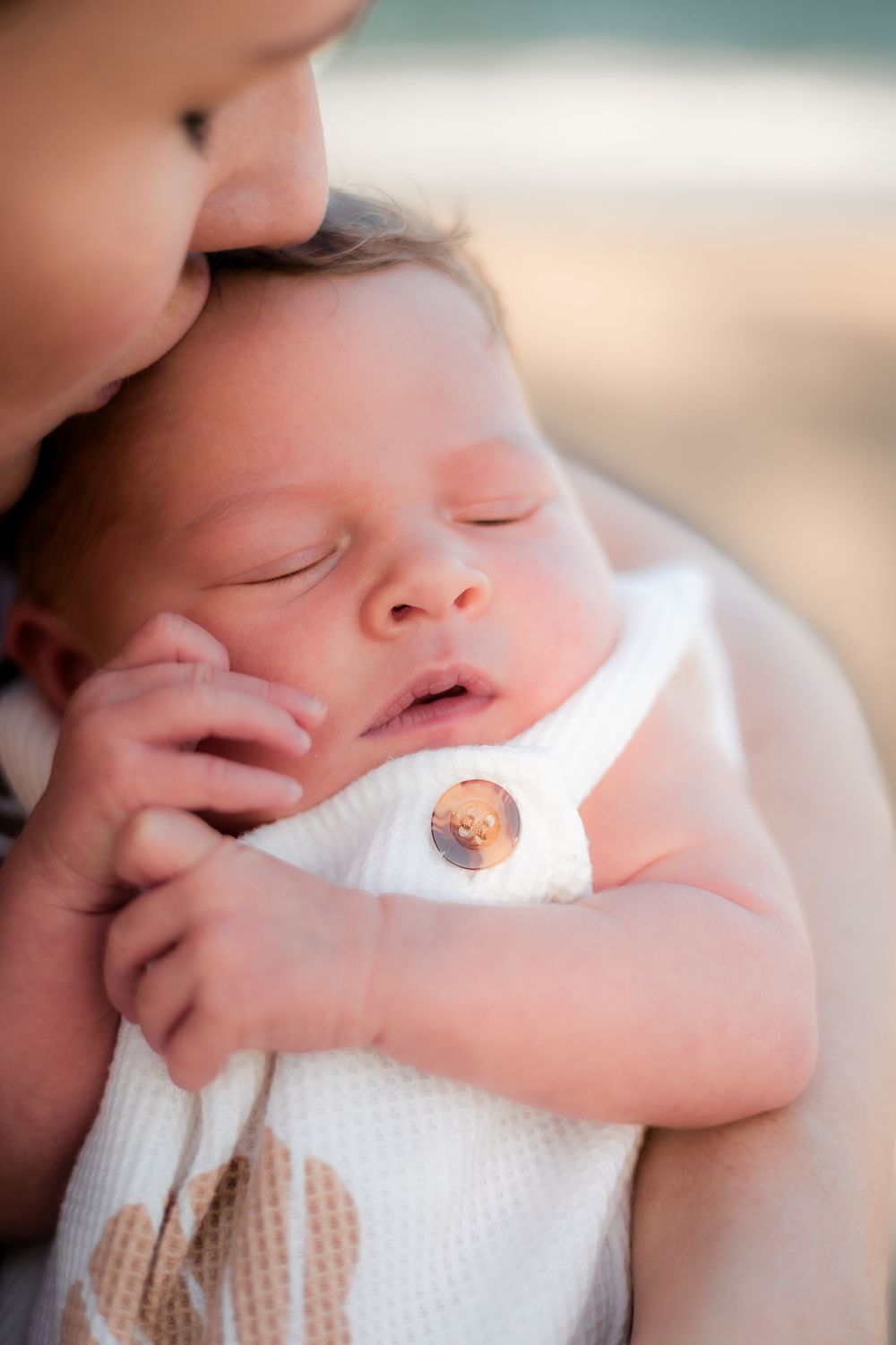 new mother kissing newborn baby during photoshoot on the beach at sunset in the Sunshine Coast