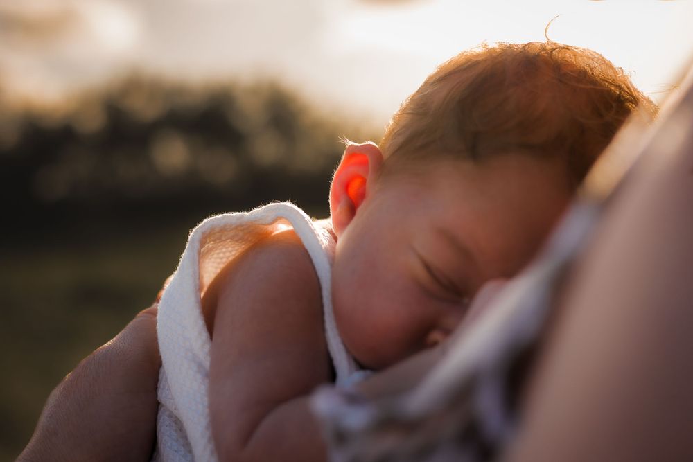 Newborn photoshoot on the beach at sunset in the Sunshine Coast with golden hour glow shining onto baby