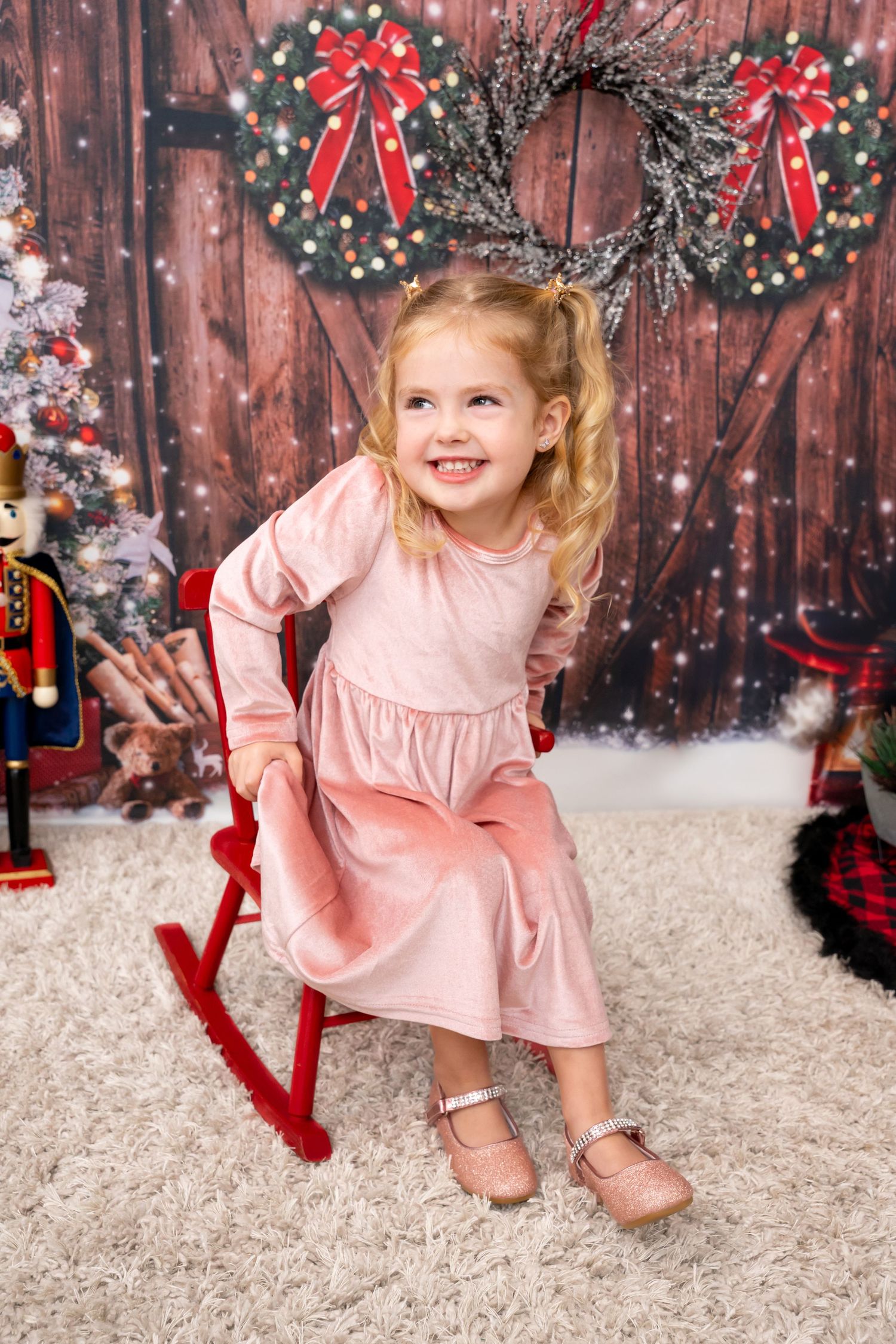 A child in a pink dress playing in a festive holiday setting with wreaths and snow.