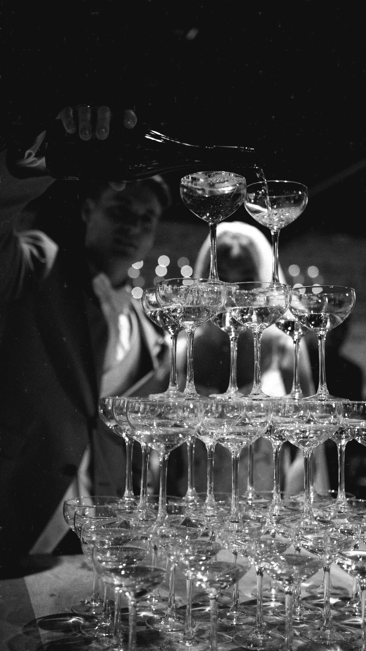 Black and white photo of a cocktail glass with confetti scattered on wooden floor.