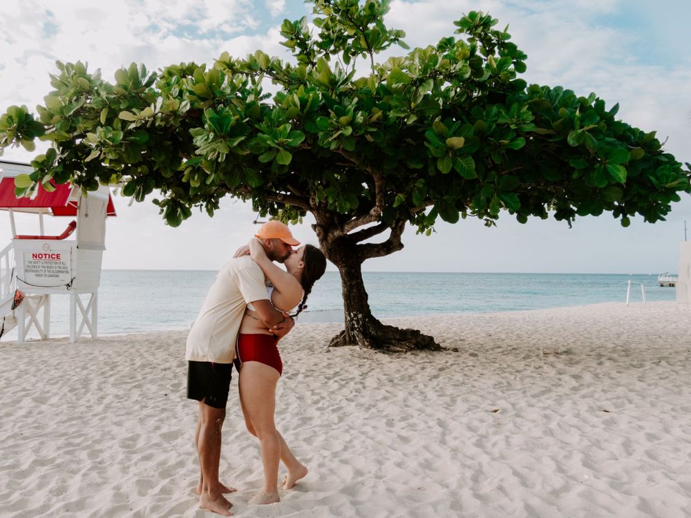 man and woman kissing in front of a tree at doctors cave in montego bay jamaica