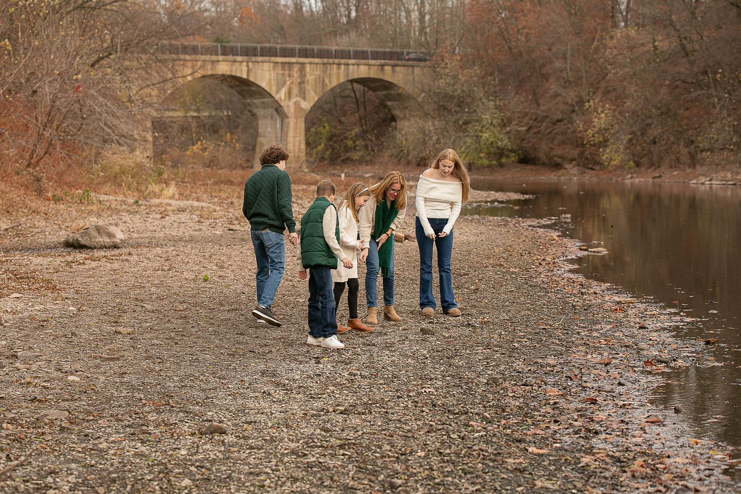 Family posing near stone bridge and creek during autumn photoshoot.