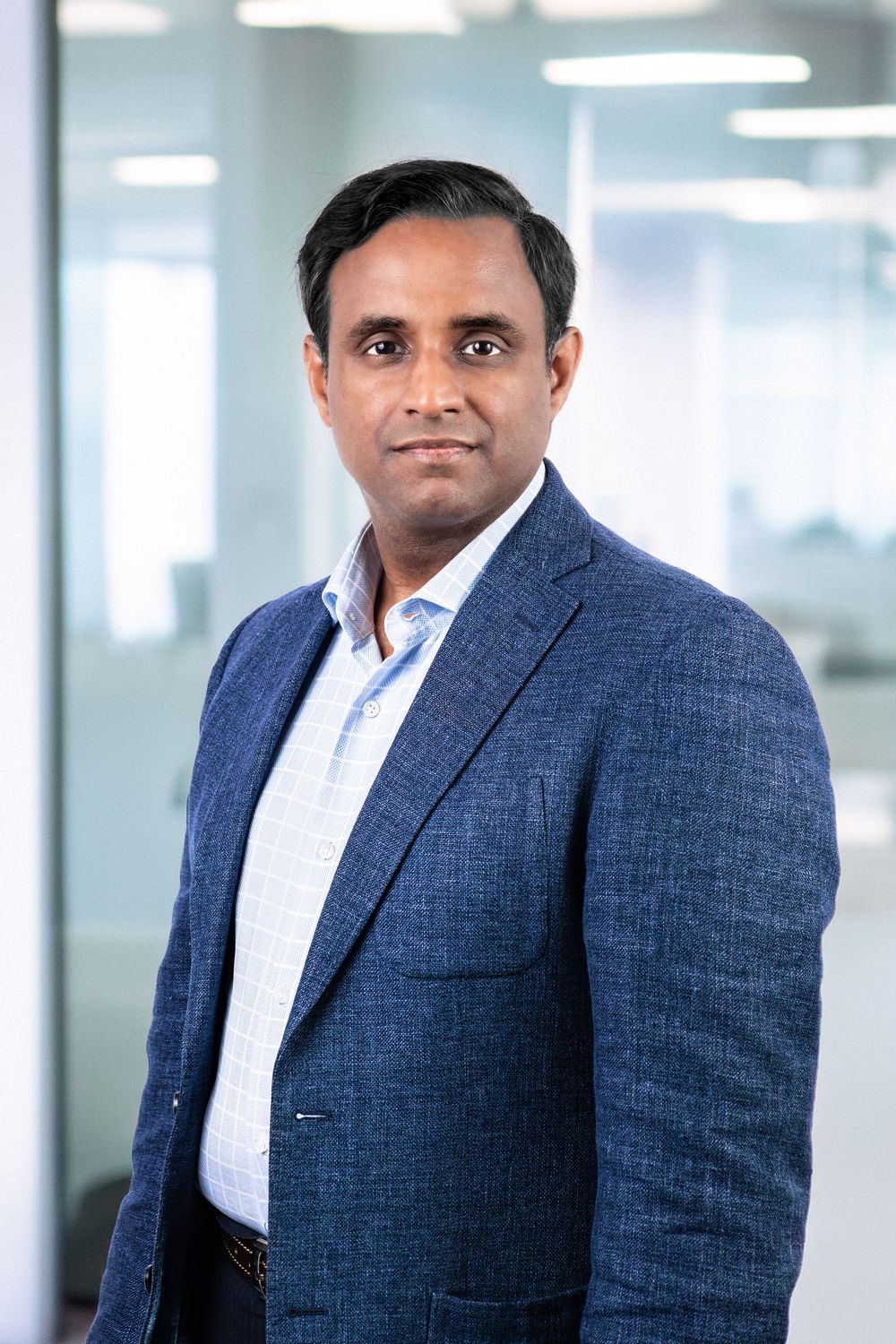 Professional man in blue blazer poses confidently in modern office setting for corporate headshot photo.