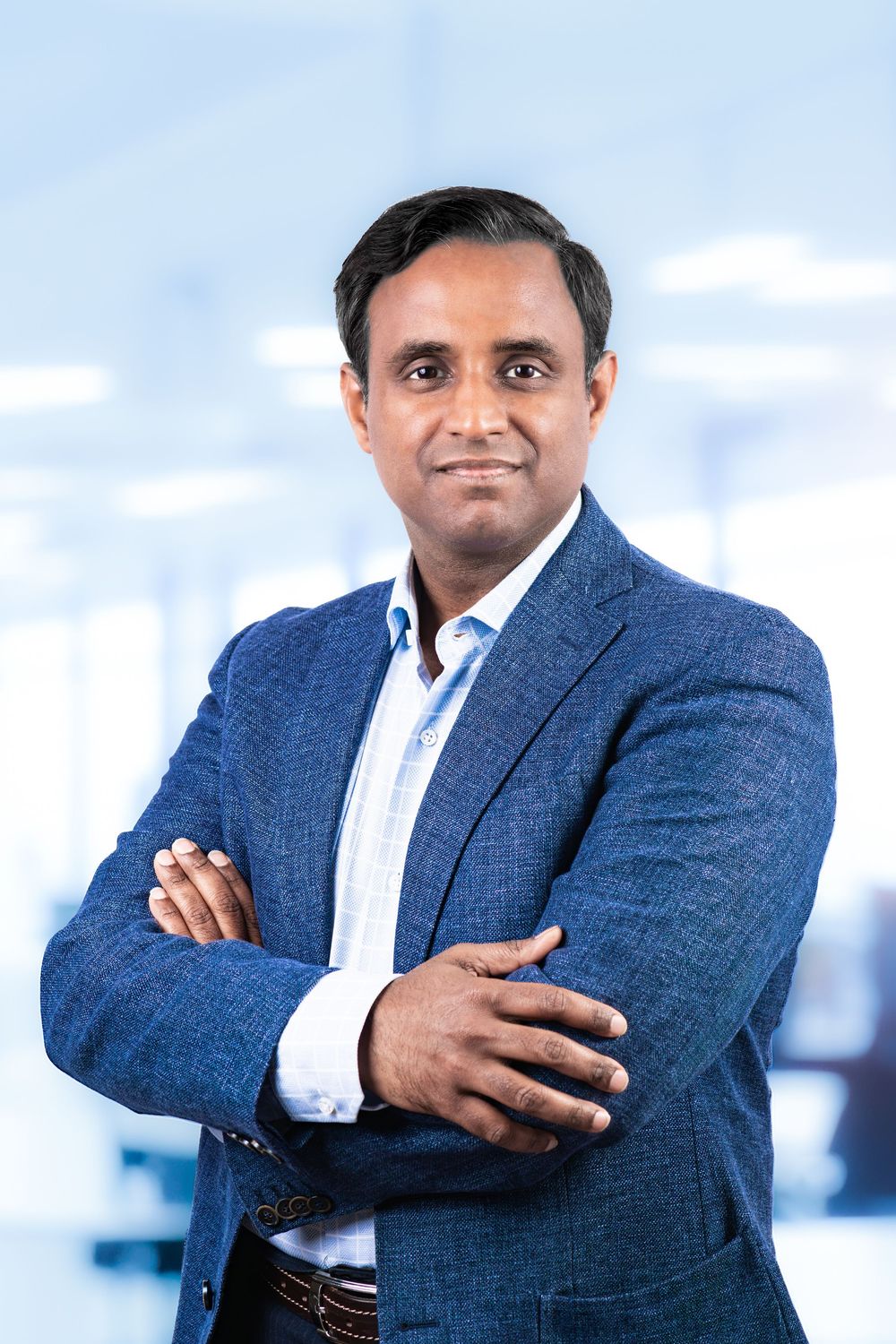 Professional man in blue blazer with arms crossed smiling confidently in a modern office setting.