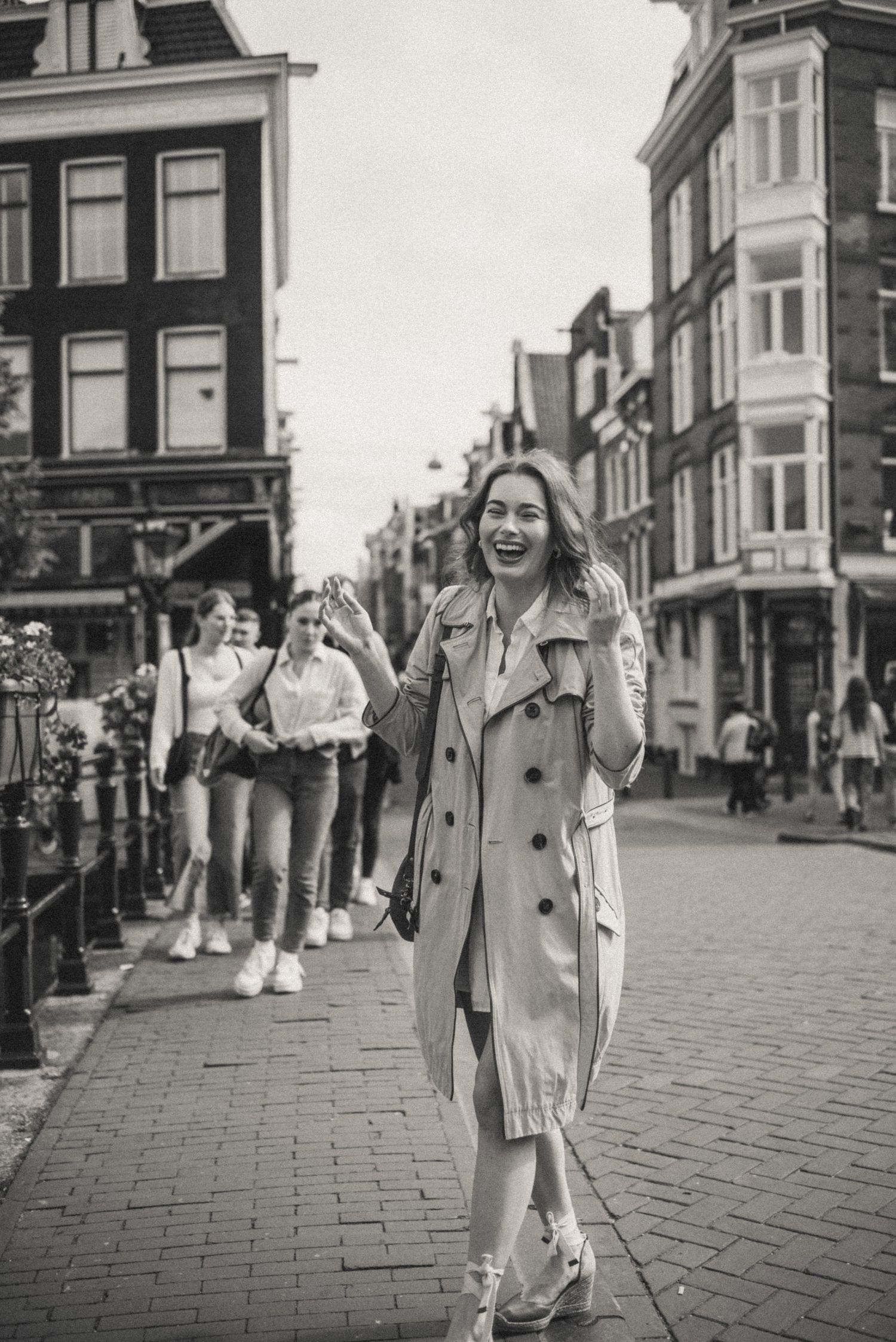 Black and white candid photo of a woman laughing on a bridge in Amsterdam – raw and authentic emotions.