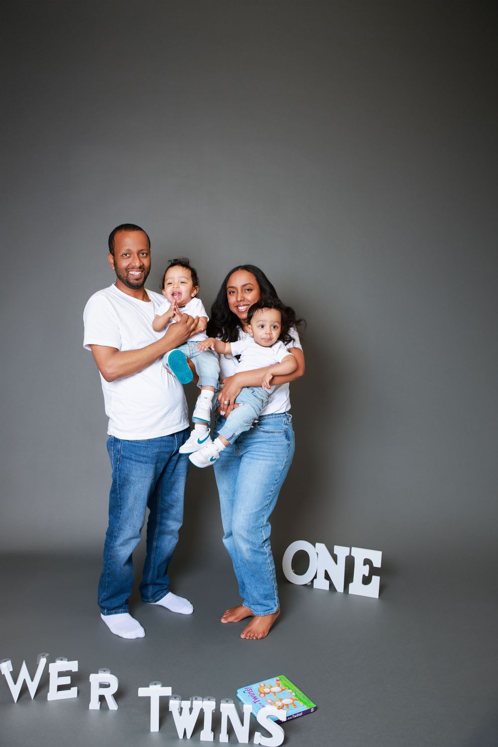 Family portrait with twins and 'ONE' text decoration against grey background.
